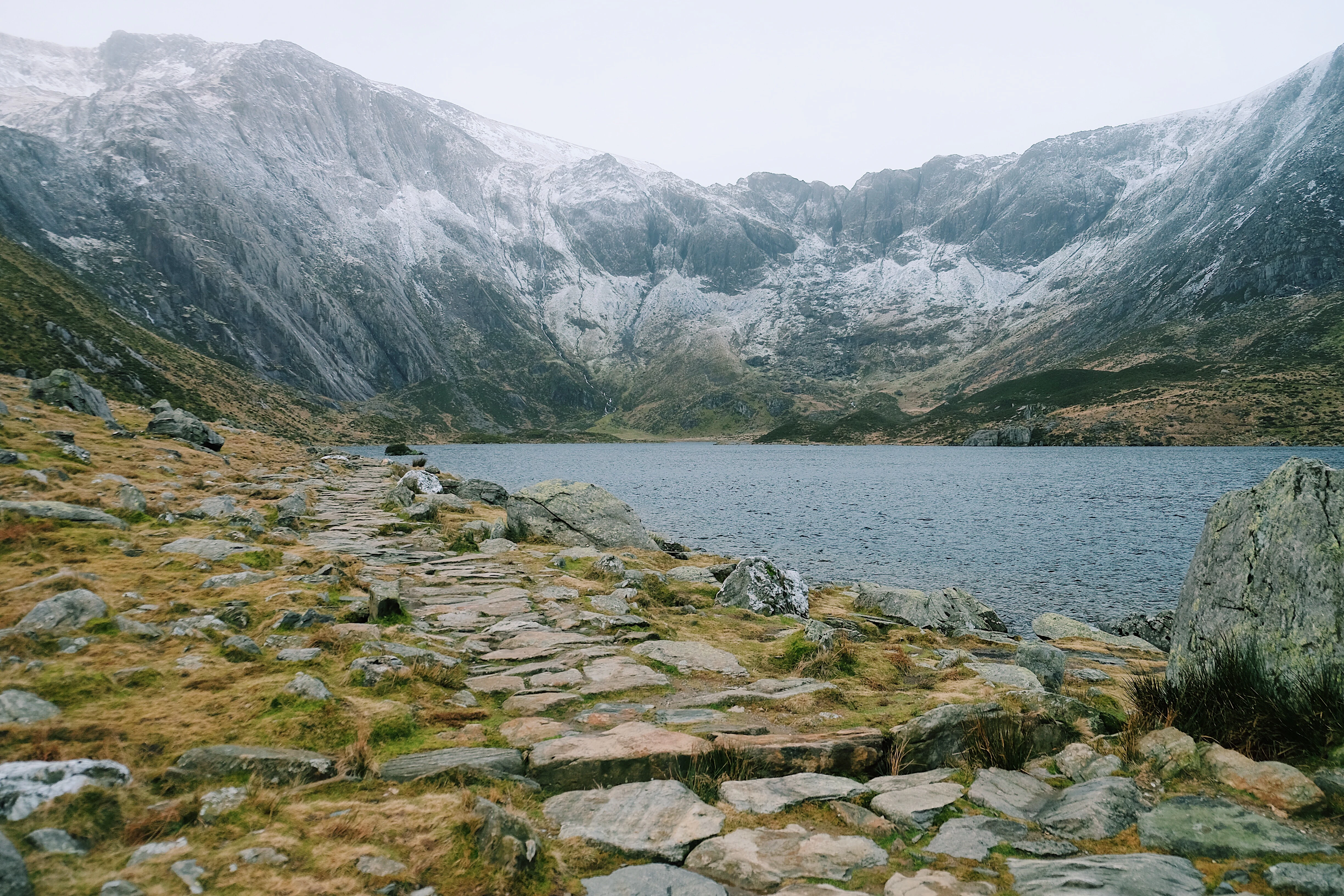 Stone path leading to a lake with snow-covered mountains in the background