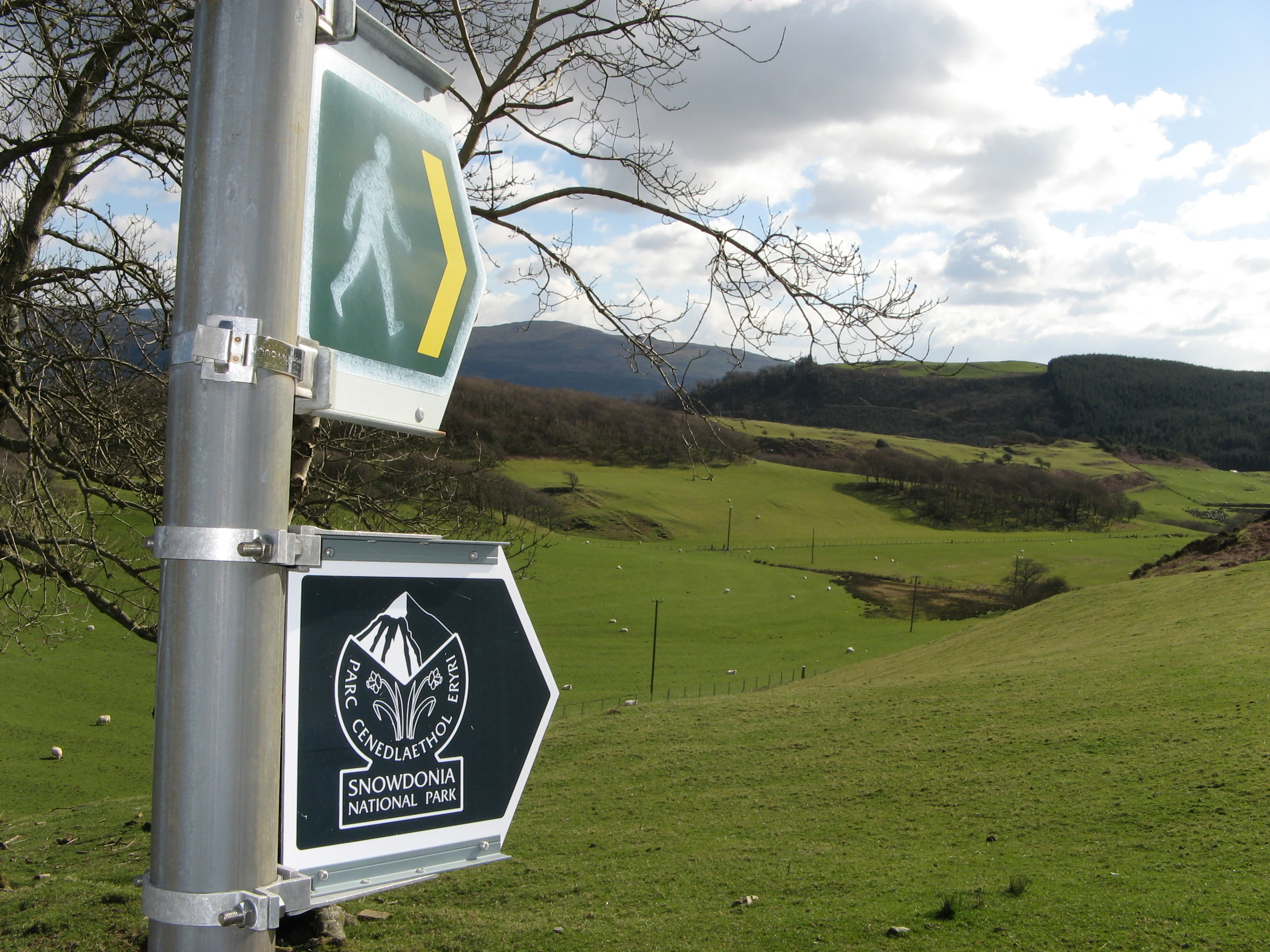 Signpost with Snowdonia National Park walking trail signs showing green hills and mountains