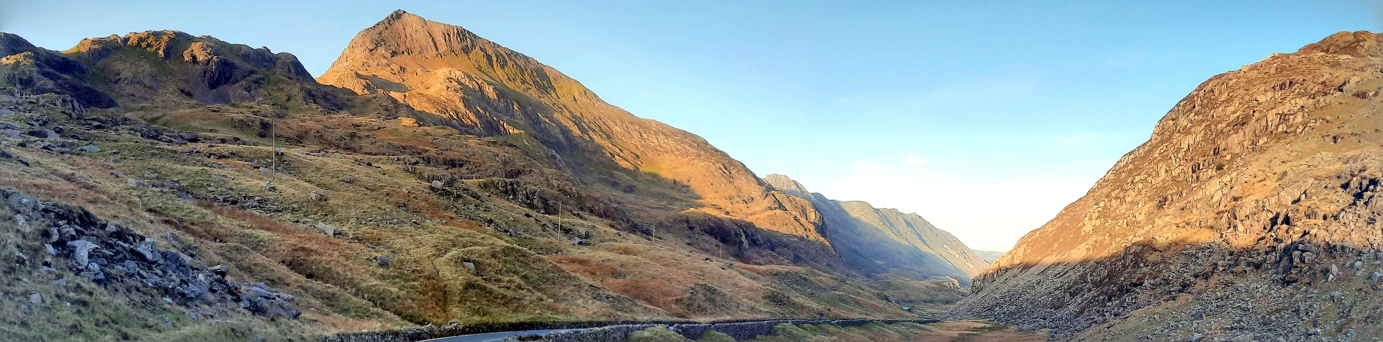 Panoramic view of Llanberis Pass with rocky mountains and valley under clear blue sky in autumn