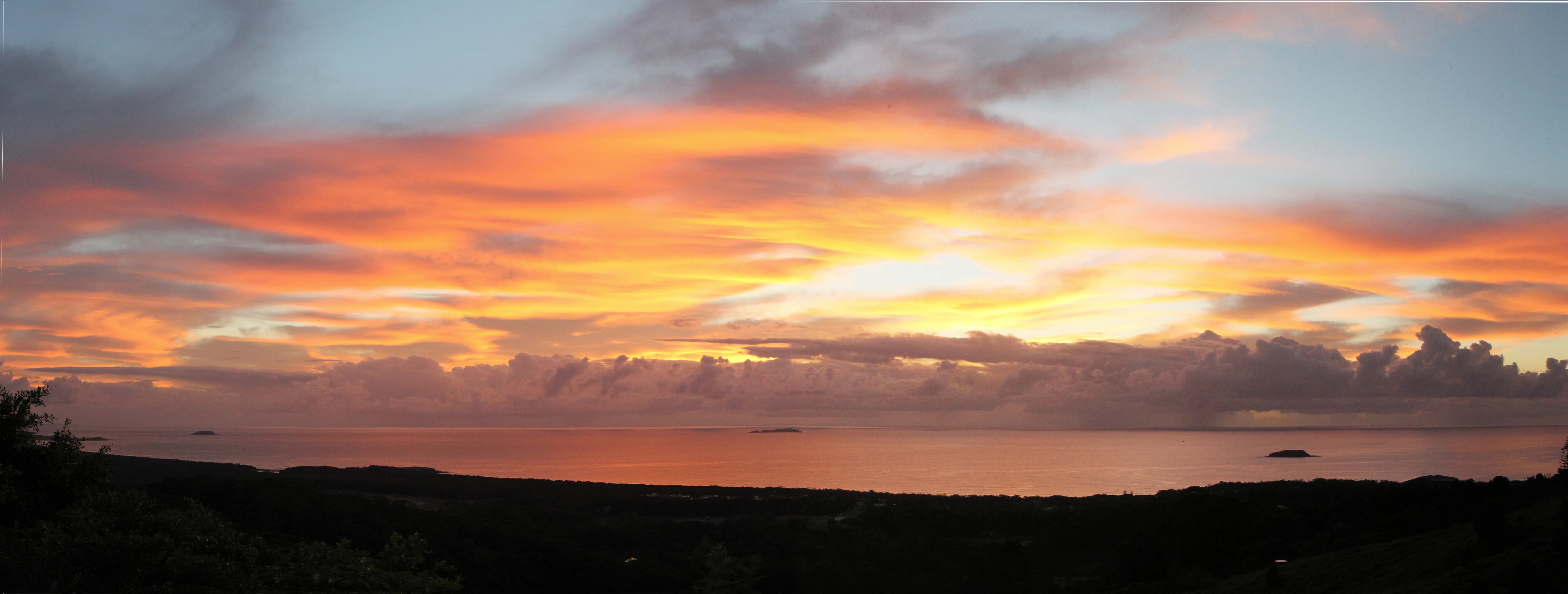 Vista panorámica de un vibrante amanecer sobre el océano con siluetas oscuras del terreno costero en primer plano.