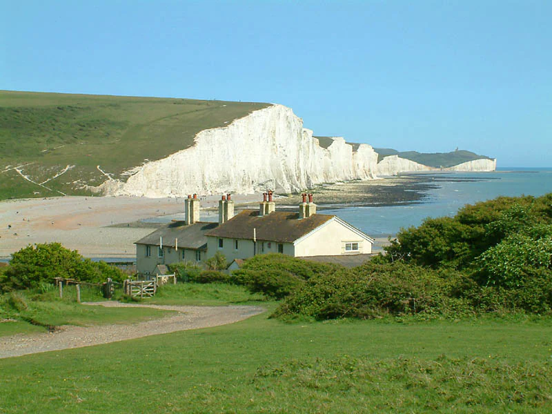 White chalk cliffs, coastguard cottages, green hillside, sandy beach, and ocean under a clear blue sky