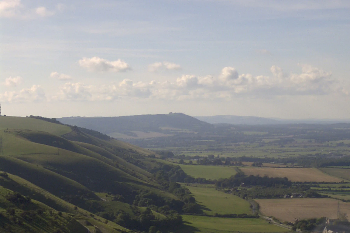 Chalk downland hills and rolling green valleys under a partly cloudy sky