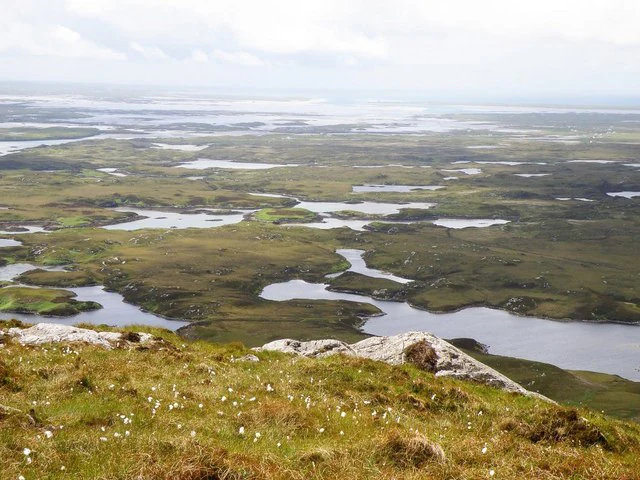 A high-angle view looking over a sprawling, boggy coastal landscape in North Uist, Scotland, characterized by numerous small lochs and rocky outcrops under an overcast sky.