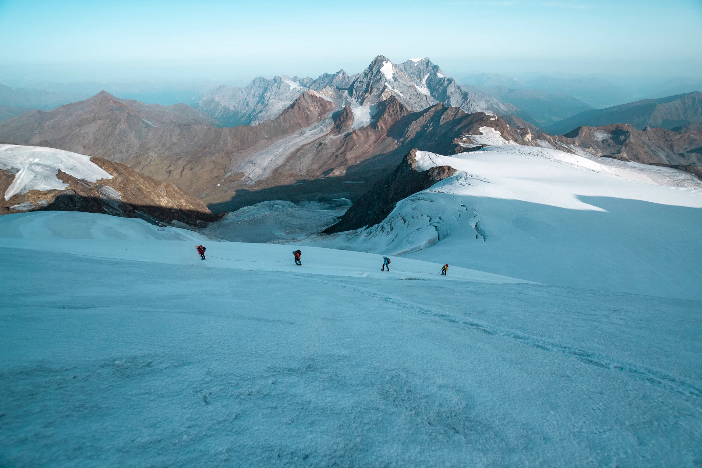 Hikers walking on a glacier with mountain peaks in the background