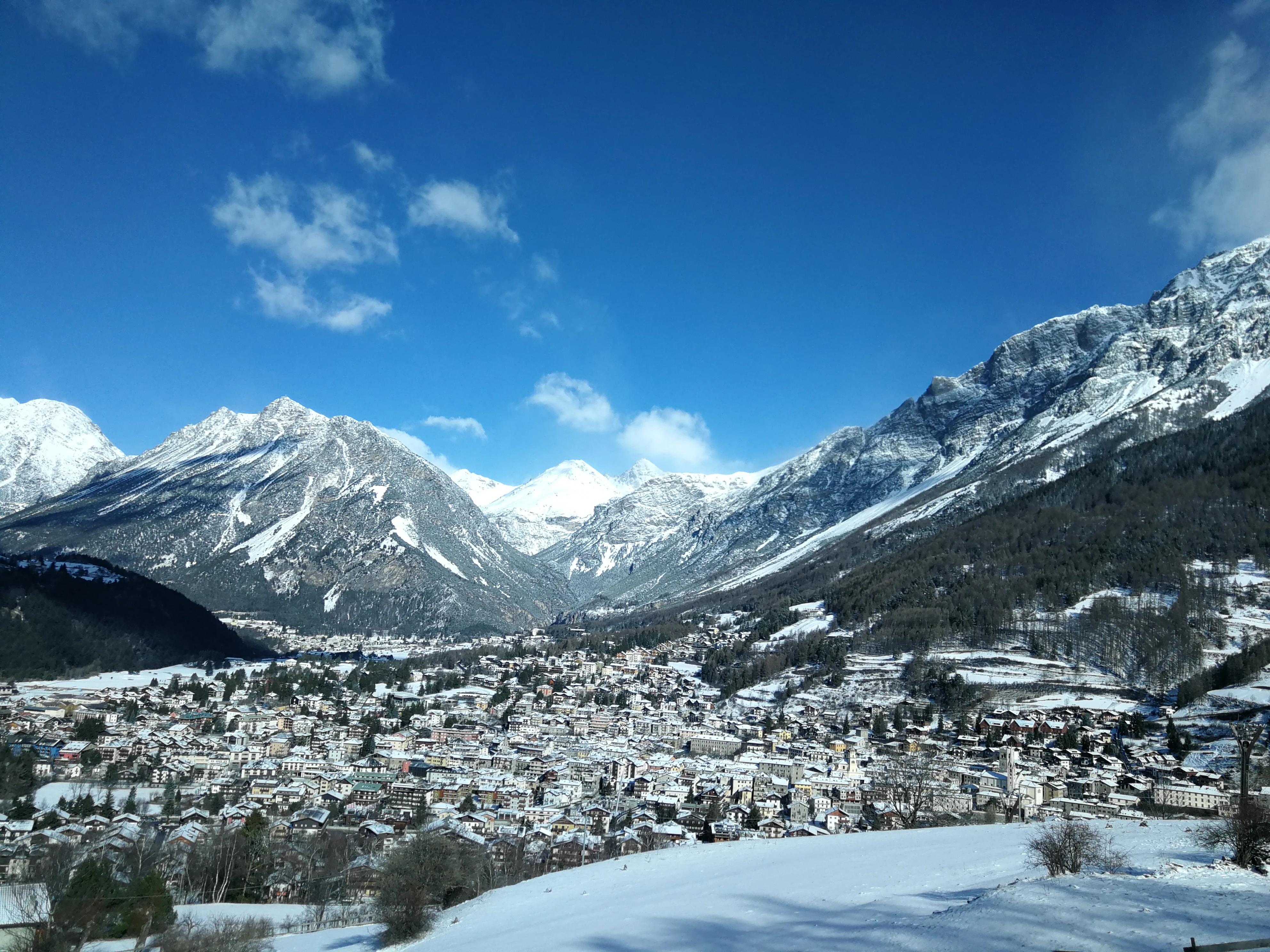 Panoramic view of Bormio town with snow-capped mountains under a clear blue sky