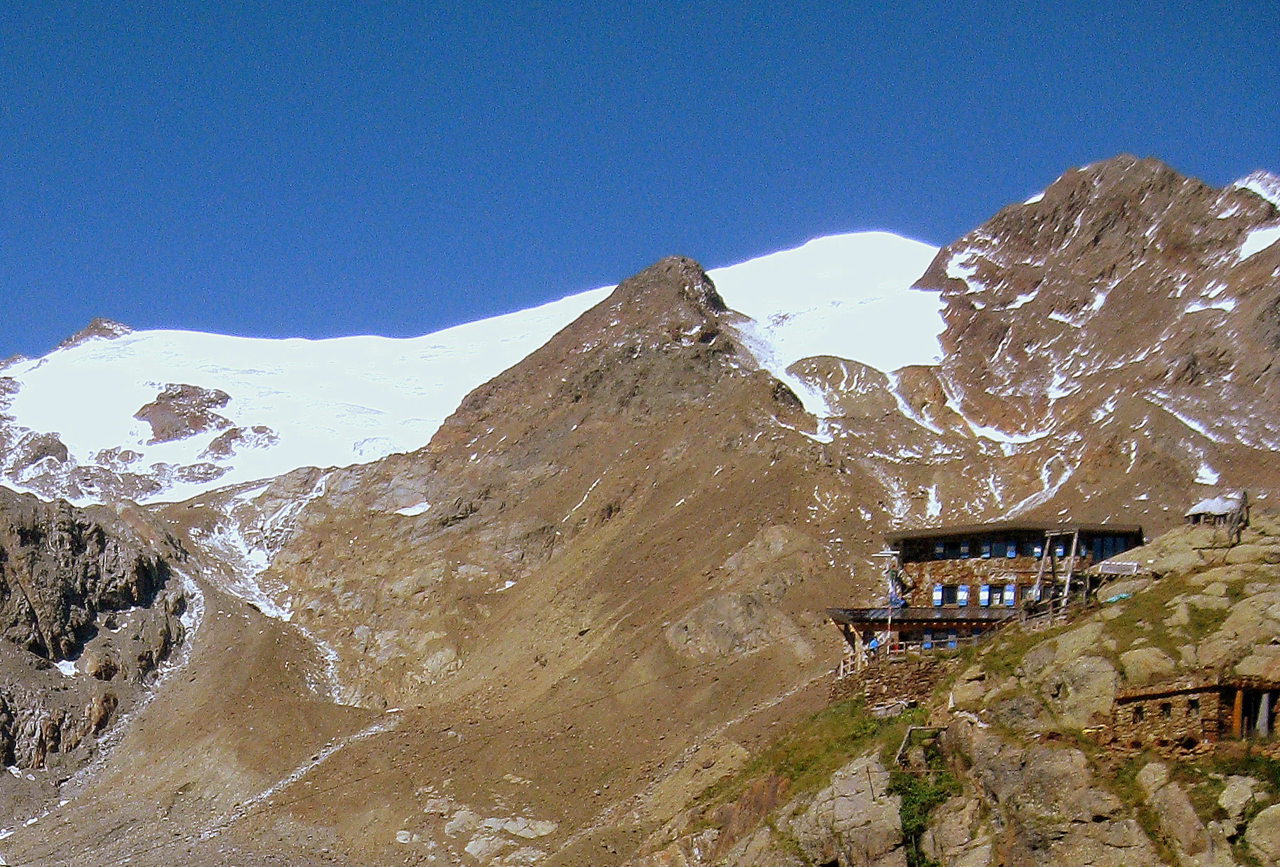 Mountain hut Rifugio Larcher on rocky terrain with snow-covered mountains in the background