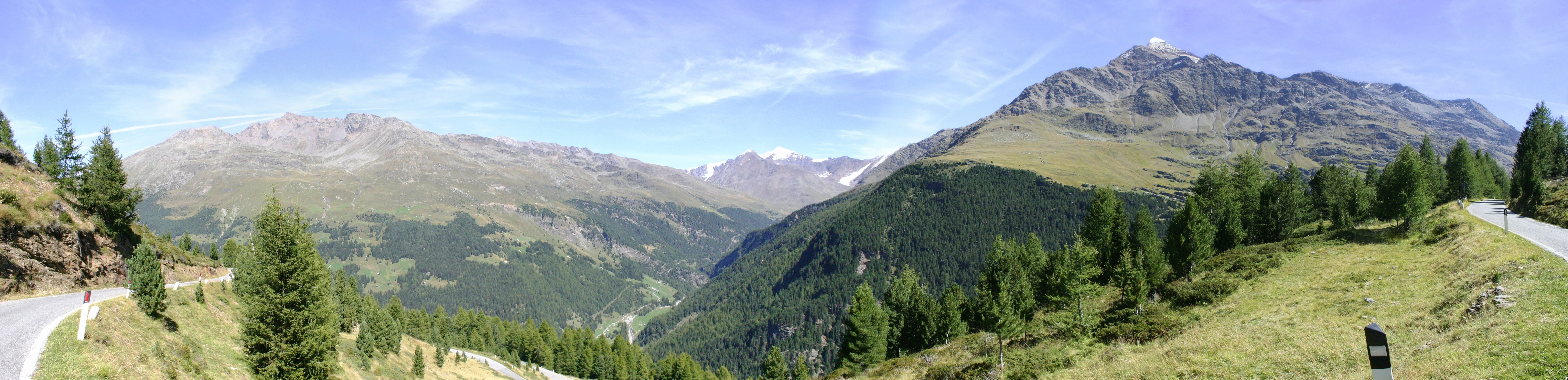 Panoramic view of Gavia Pass with mountain ranges, green valleys, and a winding road under a clear blue sky