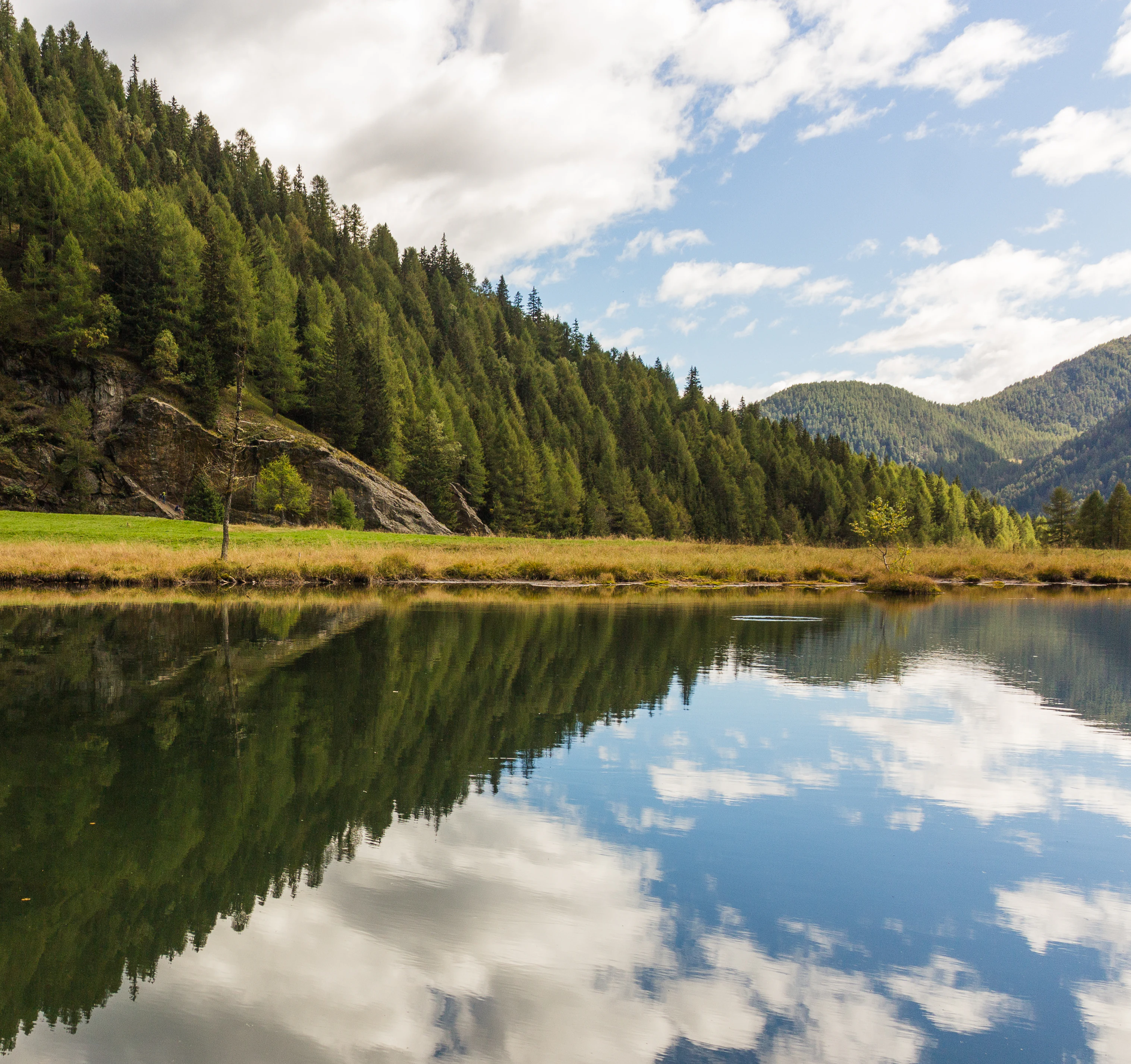 A lake reflecting a forested mountain landscape with clear blue sky and clouds