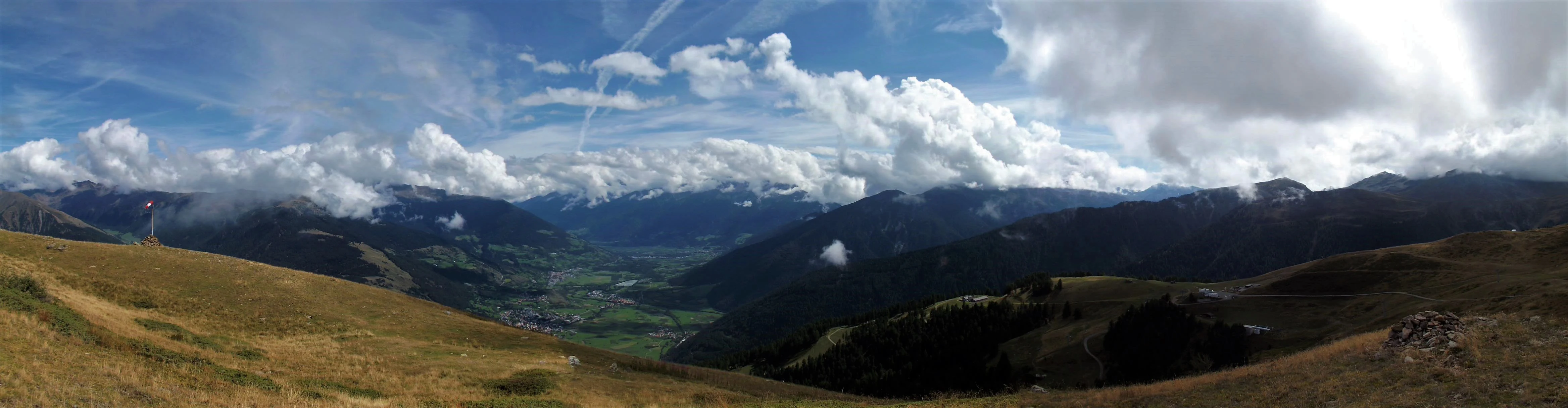 Panoramic view of mountainous terrain with valleys, scattered clouds, and distant peaks under a partly cloudy sky