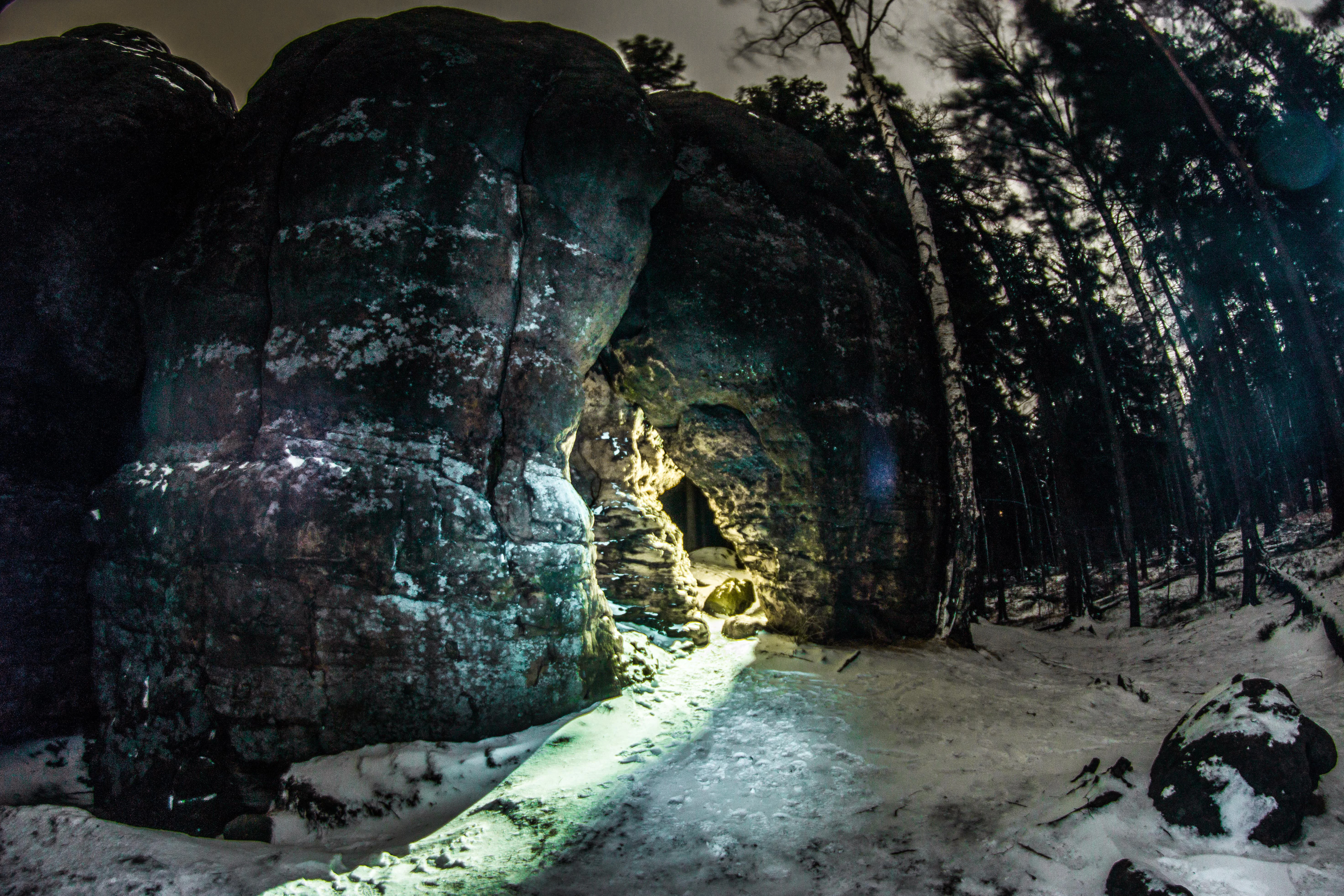 Large rock formations with an illuminated pathway through a snow-covered forest at night
