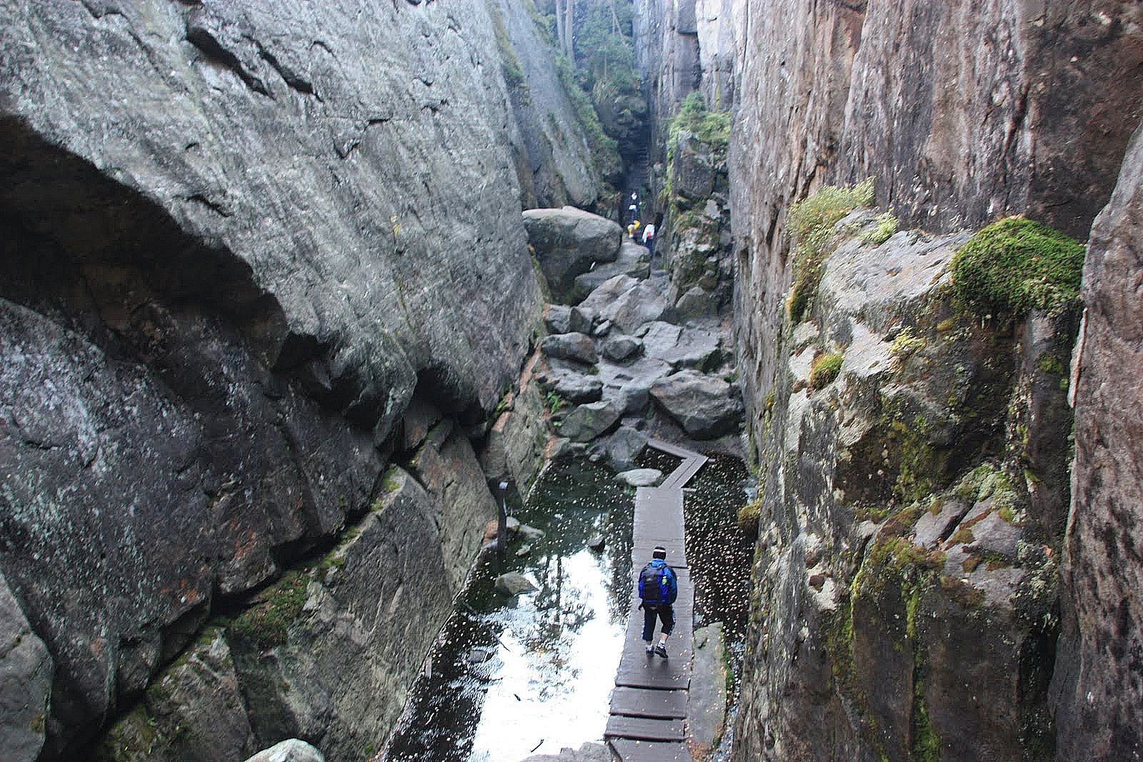 Person hiking on wooden pathway between rocky cliffs with a stream below