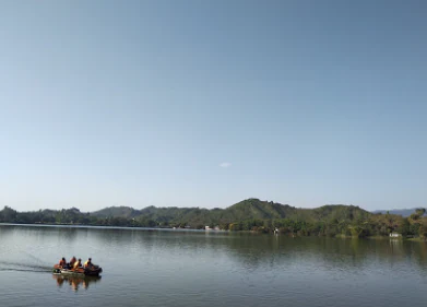 Una pequeña embarcación con pasajeros moviéndose por la superficie de un gran lago con colinas verdes onduladas al fondo bajo un cielo despejado.