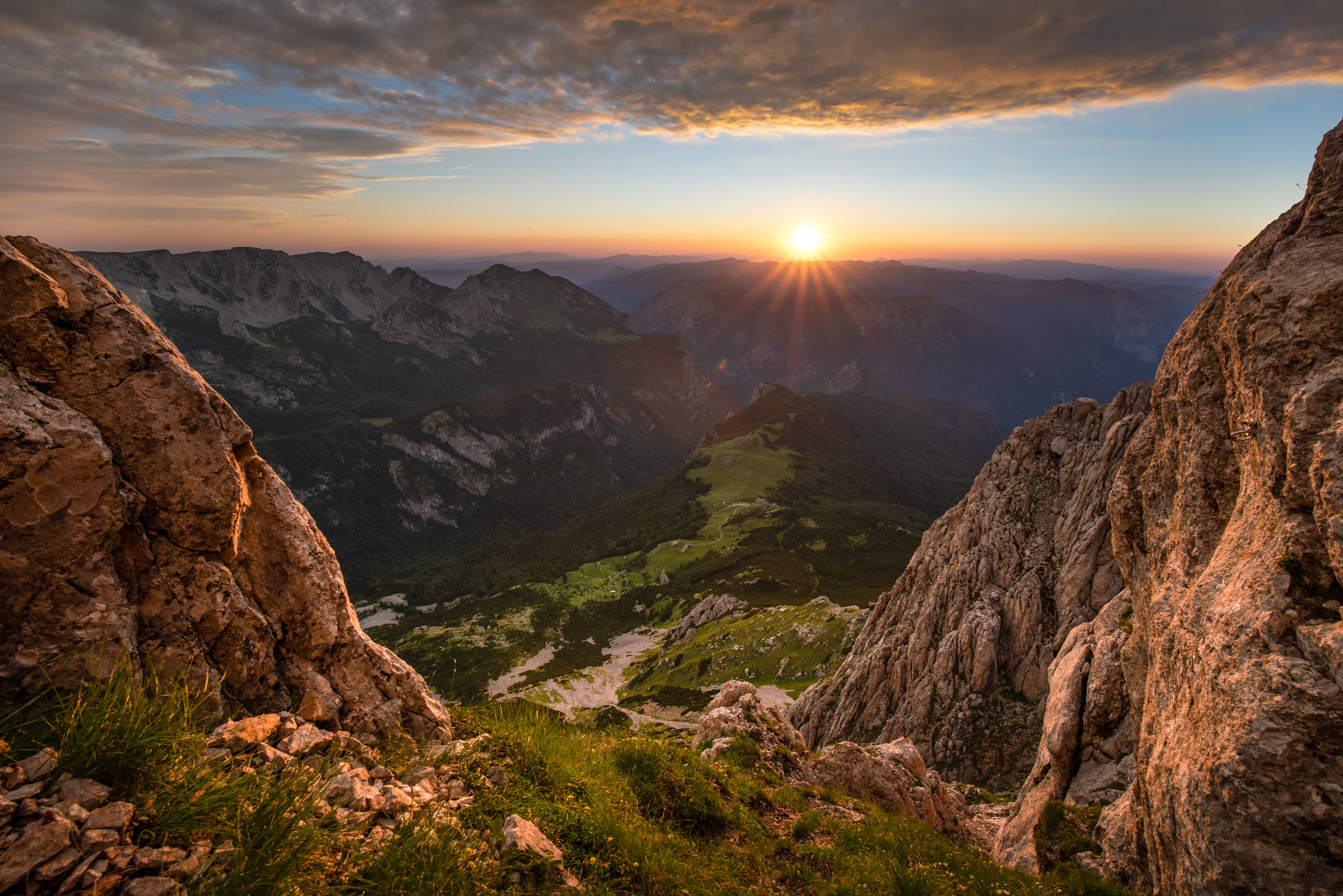 Rocky mountain peaks with a valley below, under a partly cloudy sky during sunset