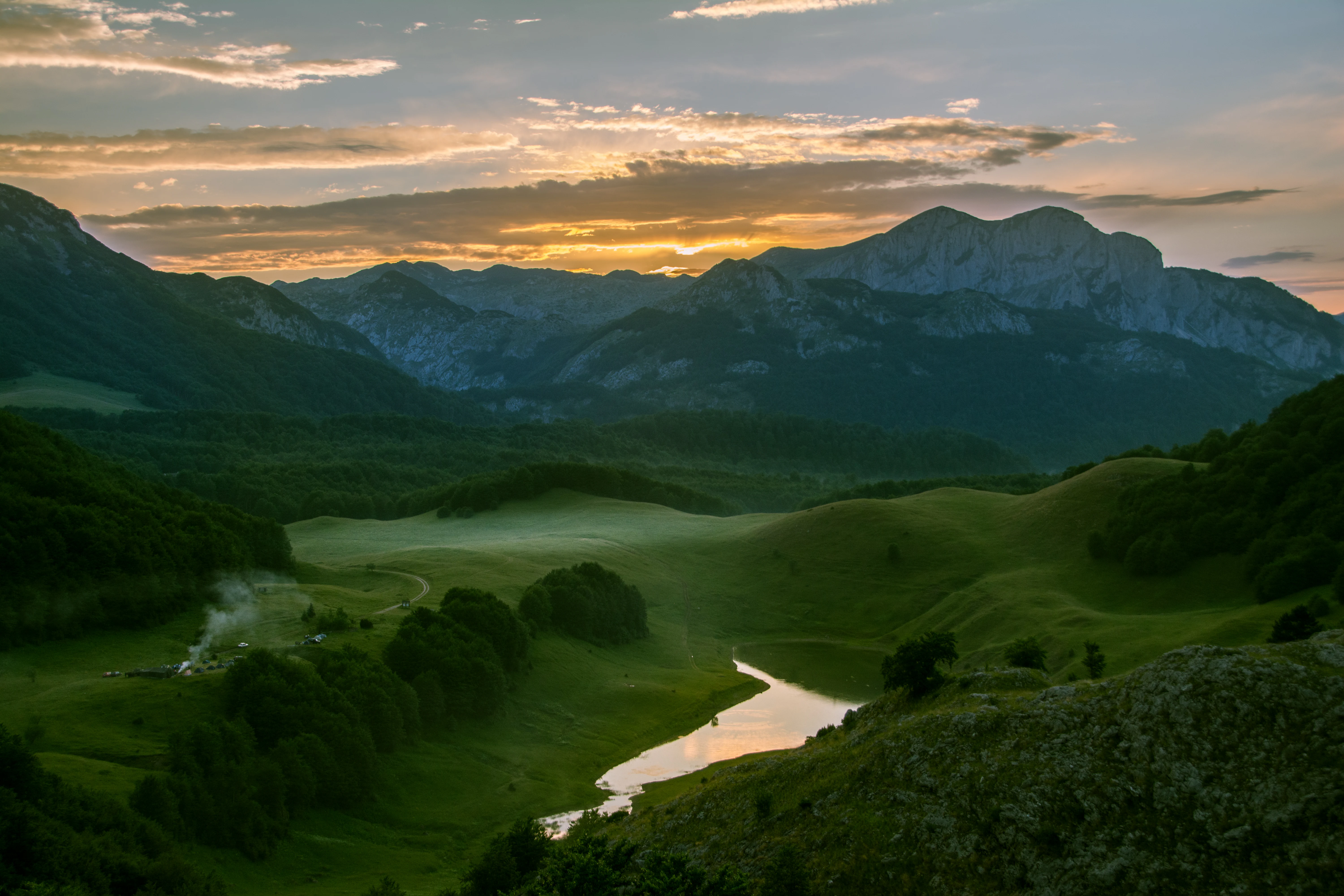 Sunset over Orlovacko Lake with green meadows and mountain peaks in the background