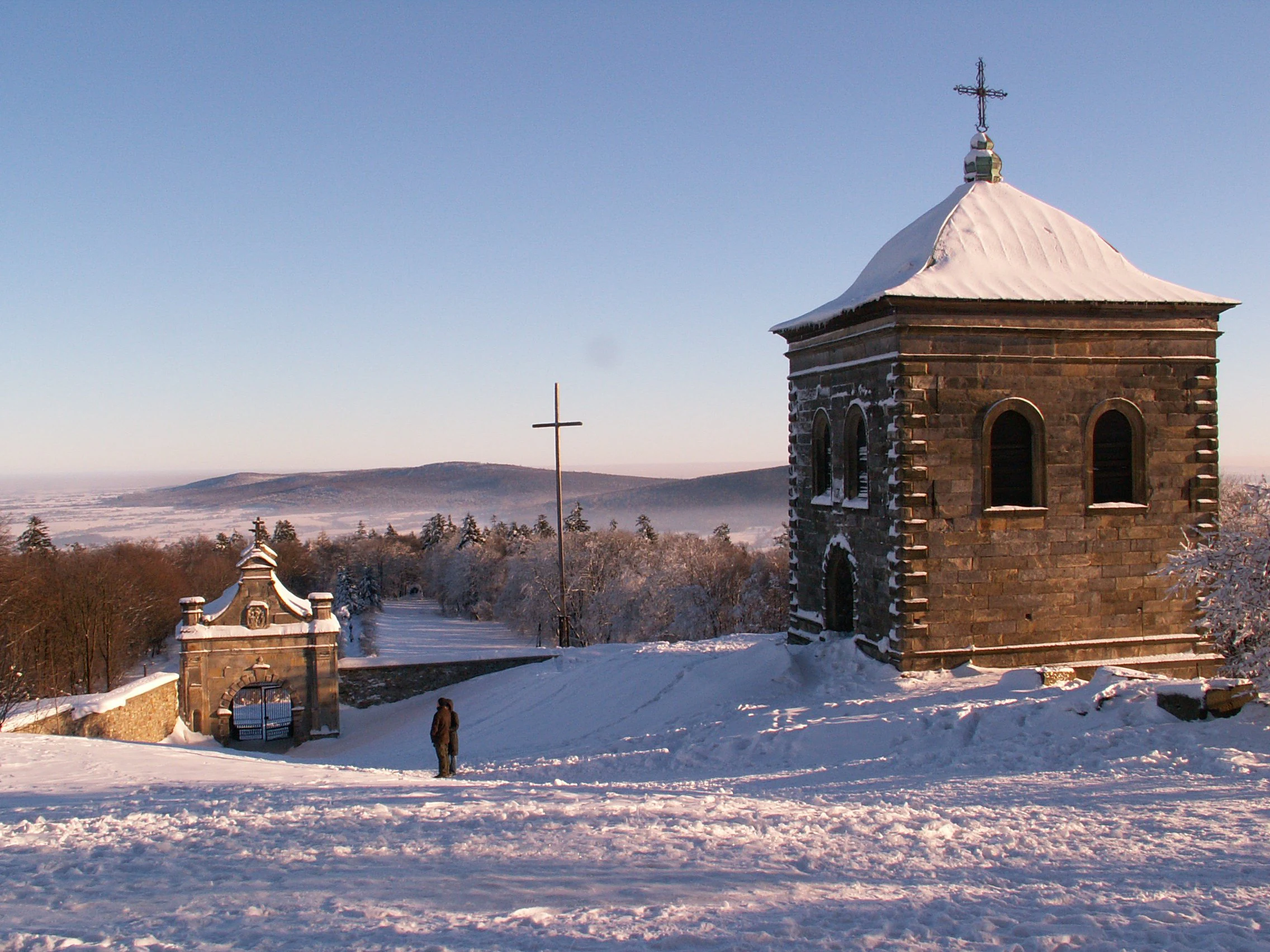 Una capilla de piedra con una cruz en lo alto y una puerta de piedra arqueada en un paisaje nevado durante el invierno.