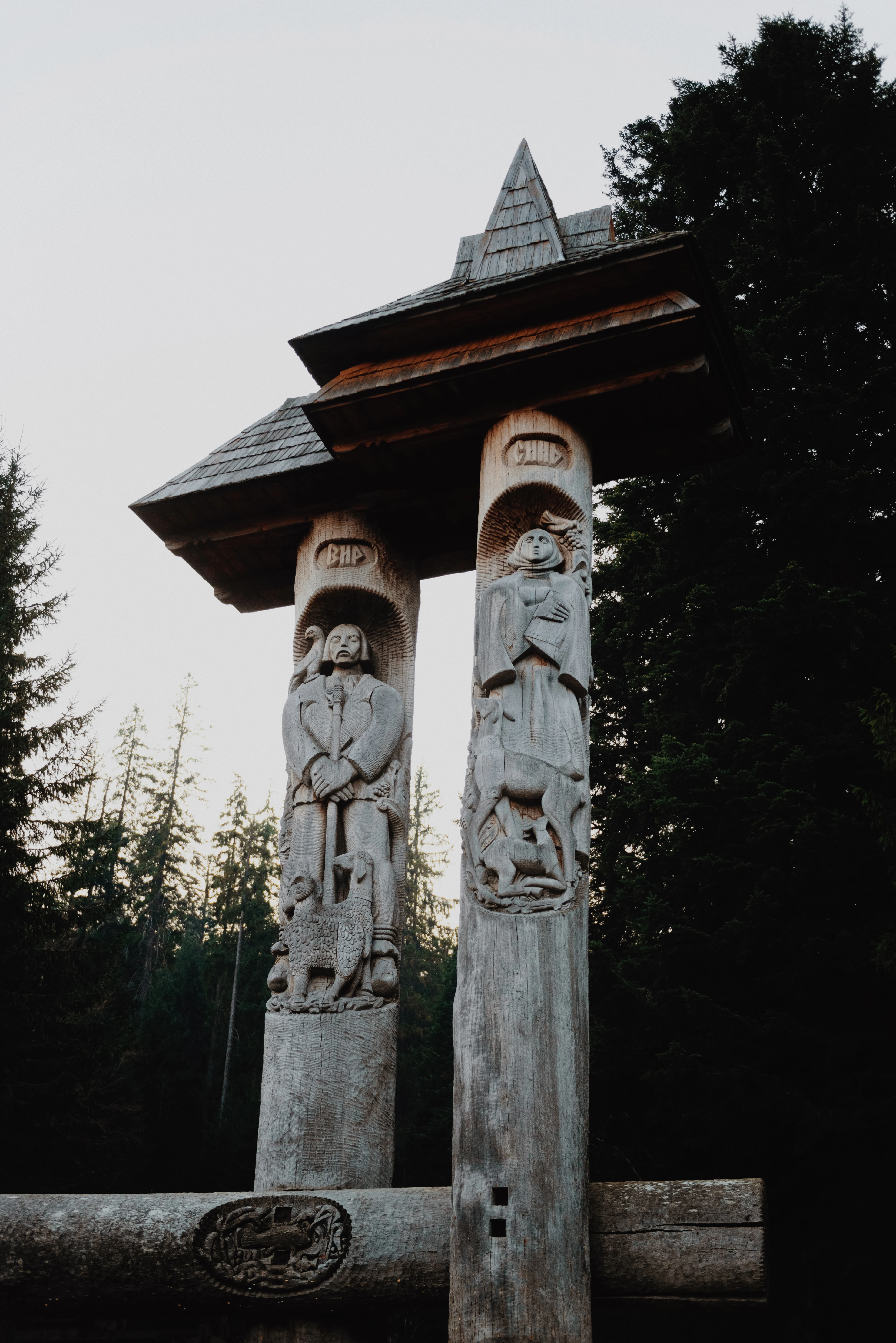 Wooden entrance sign structure with carved figures of people and animals in a forest setting