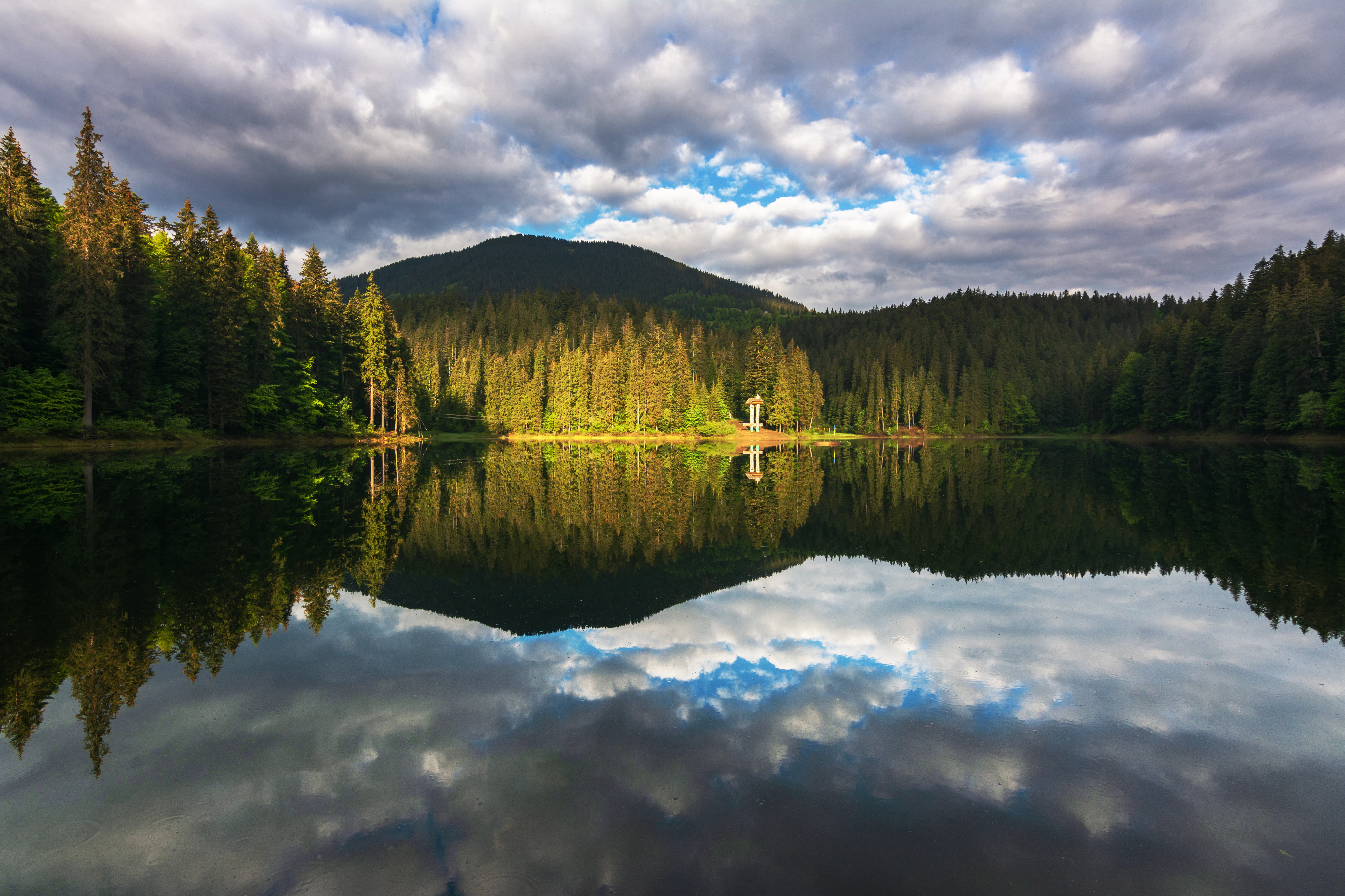 Synevyr Lake reflecting clouds and forested mountains under a partly cloudy sky