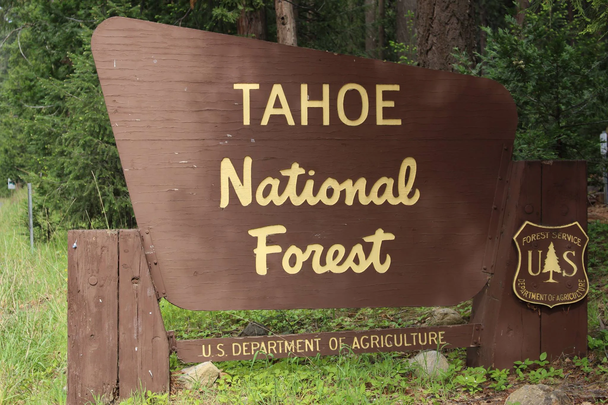 A brown wooden sign with yellow lettering reading Tahoe National Forest, positioned among green forest trees.