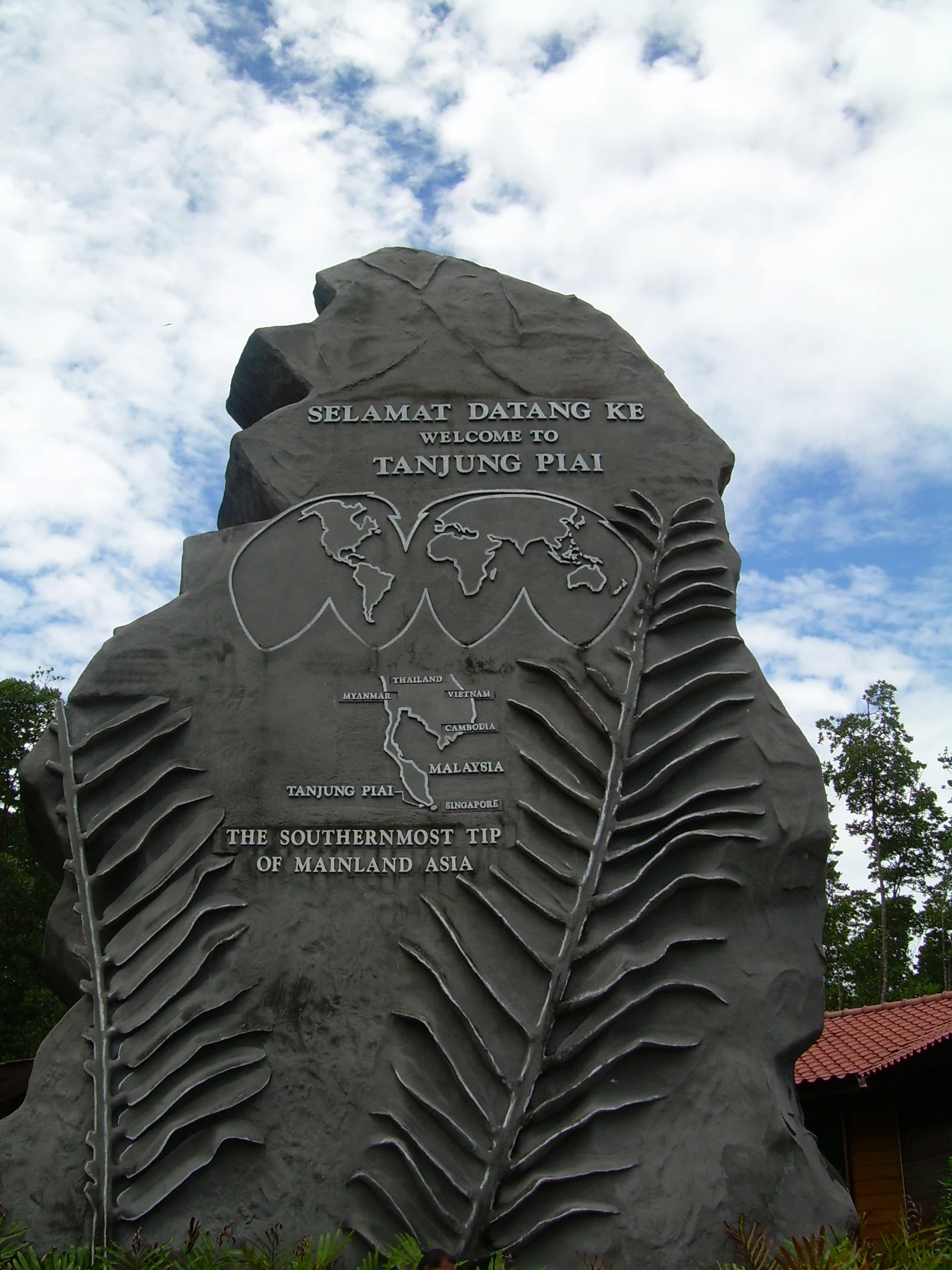 Un gran monumento de piedra gris con un mapa mundial y texto que dice Bienvenidos a Tanjung Piai, el punto más meridional de la Asia continental.