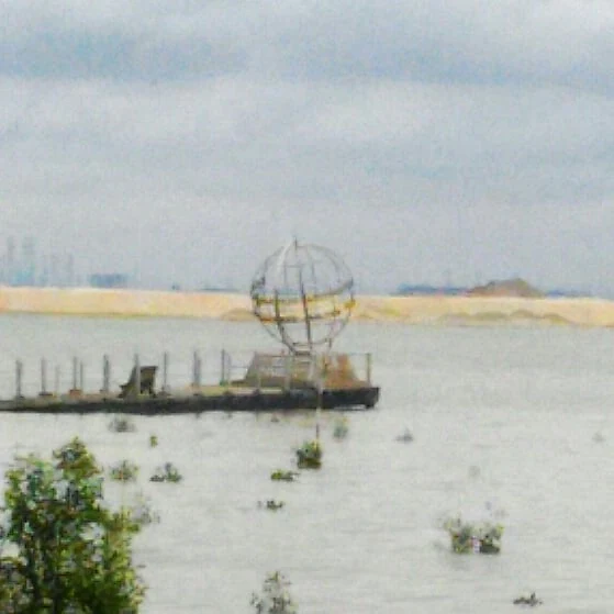 Una escultura de globo terráqueo de metal se encuentra al final de una pasarela de madera que se adentra en un cuerpo de agua, marcando el punto más meridional de la Asia continental en Tanjung Piai.