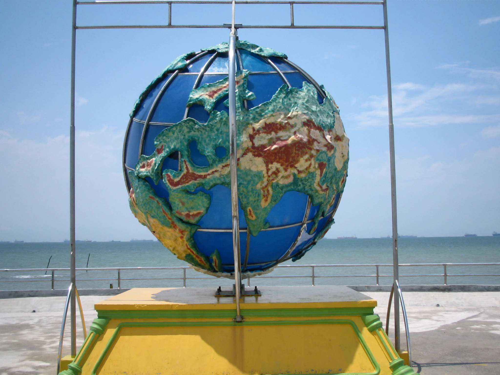 Un monumento globo sobre un pedestal amarillo con vistas al mar bajo un cielo azul.