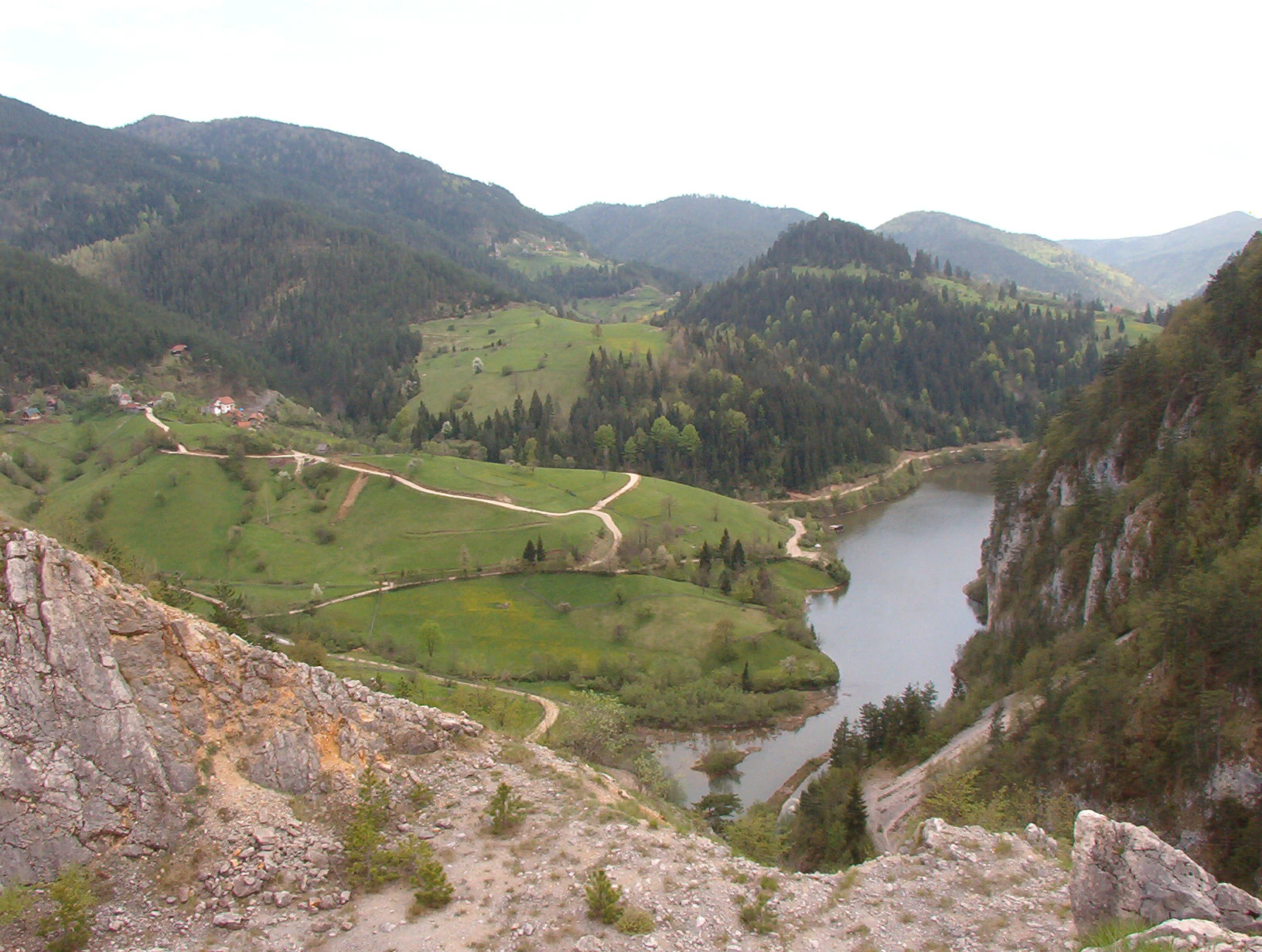Panoramic view of a lake, green hills, rocky cliffs, and distant mountains