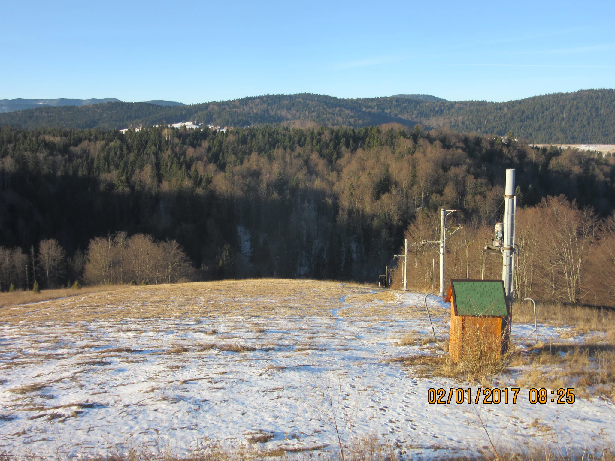 Snow-covered ski slope with ski lift poles and a small wooden structure in the background