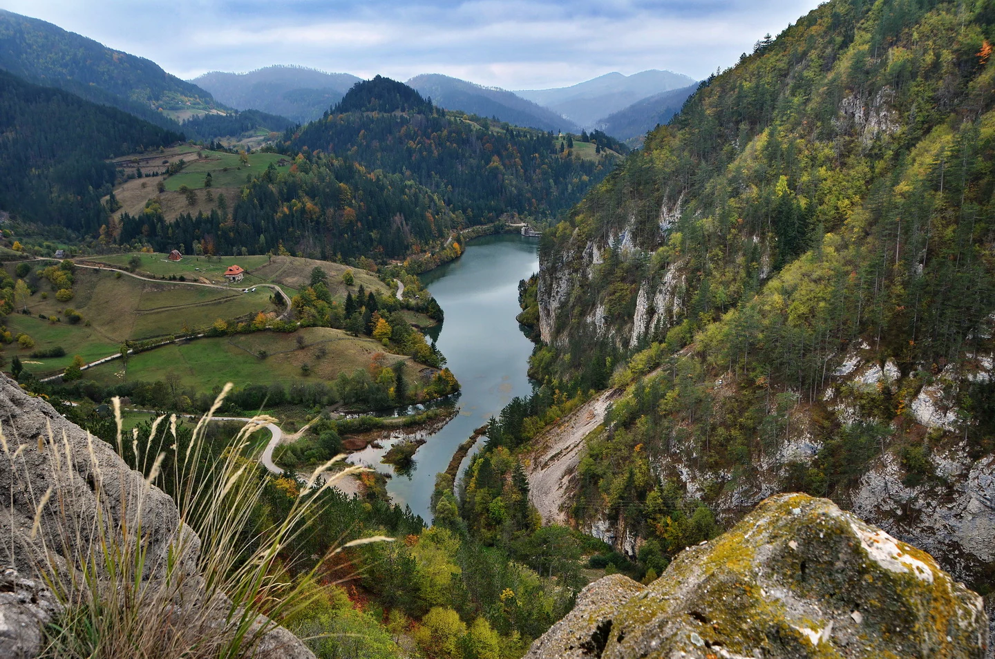 Scenic landscape featuring Spajići Lake surrounded by forested mountains, rocky cliffs, and a winding road