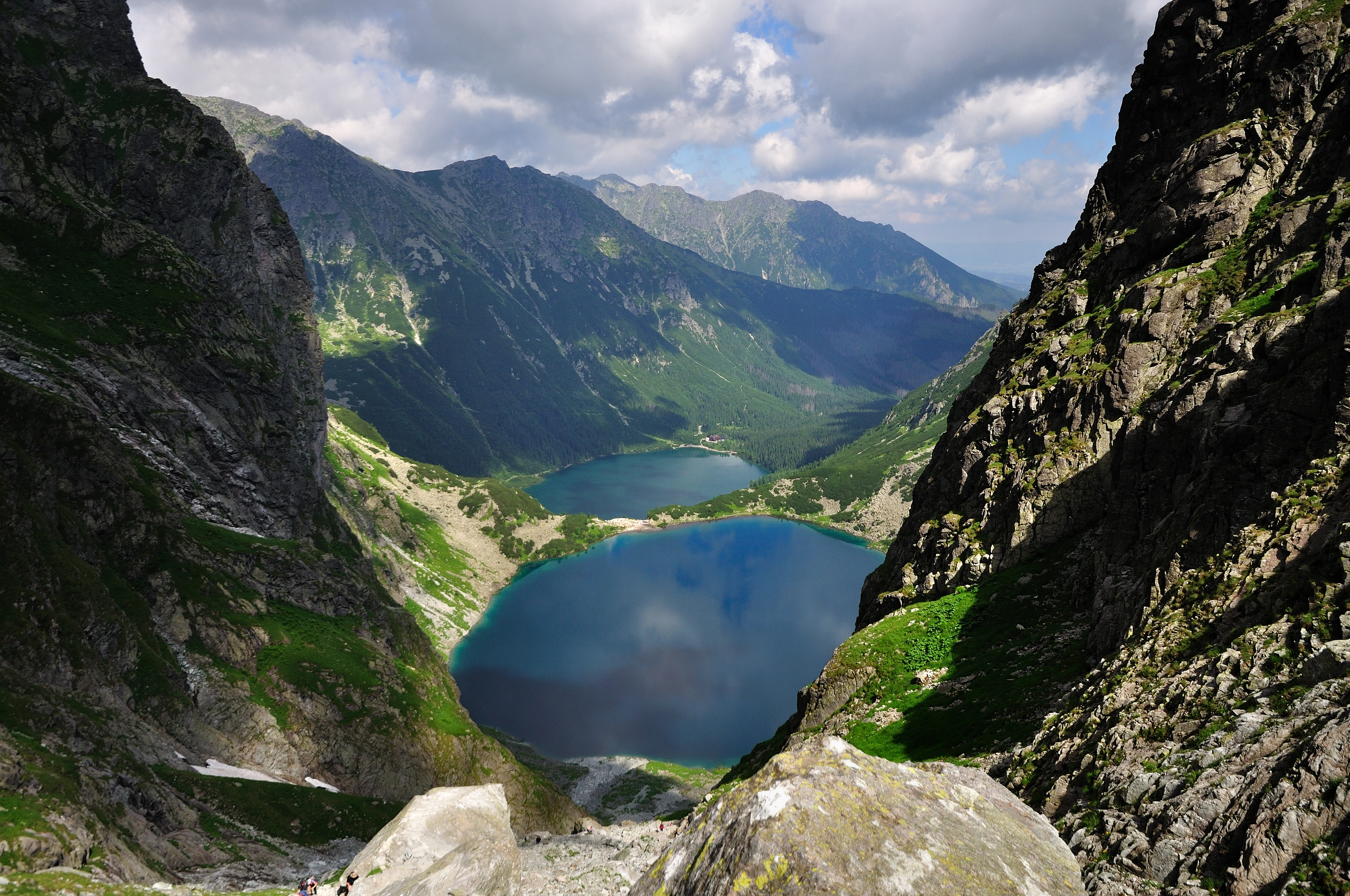 Mountain valley with two blue lakes surrounded by rocky peaks and green slopes under a partly cloudy sky