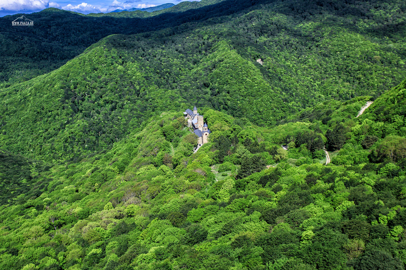 Aerial view of dense green forests covering rolling mountains with a small structure visible on a hilltop