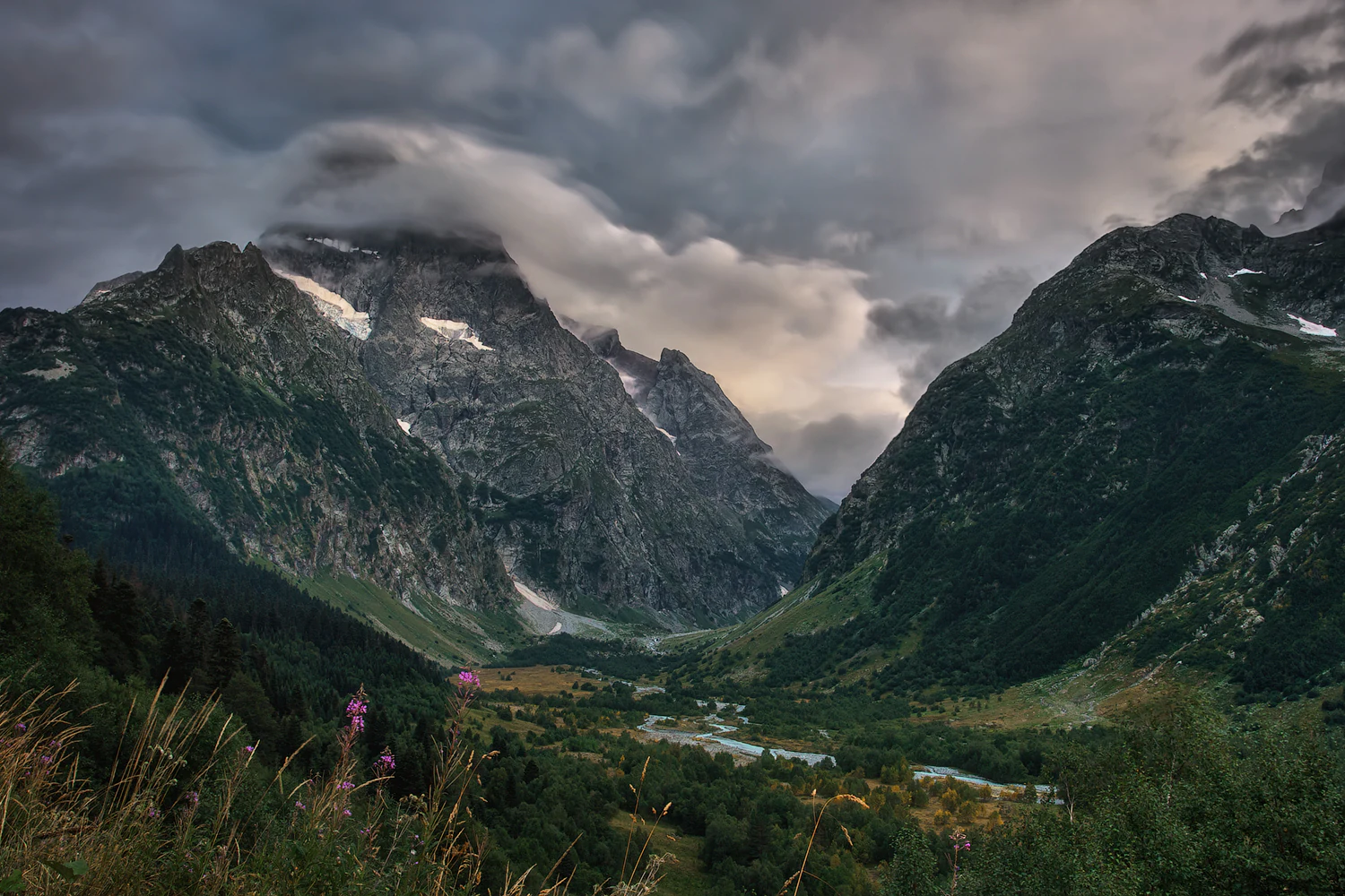 Rugged mountains with patches of snow, green valleys, and a partly cloudy sky