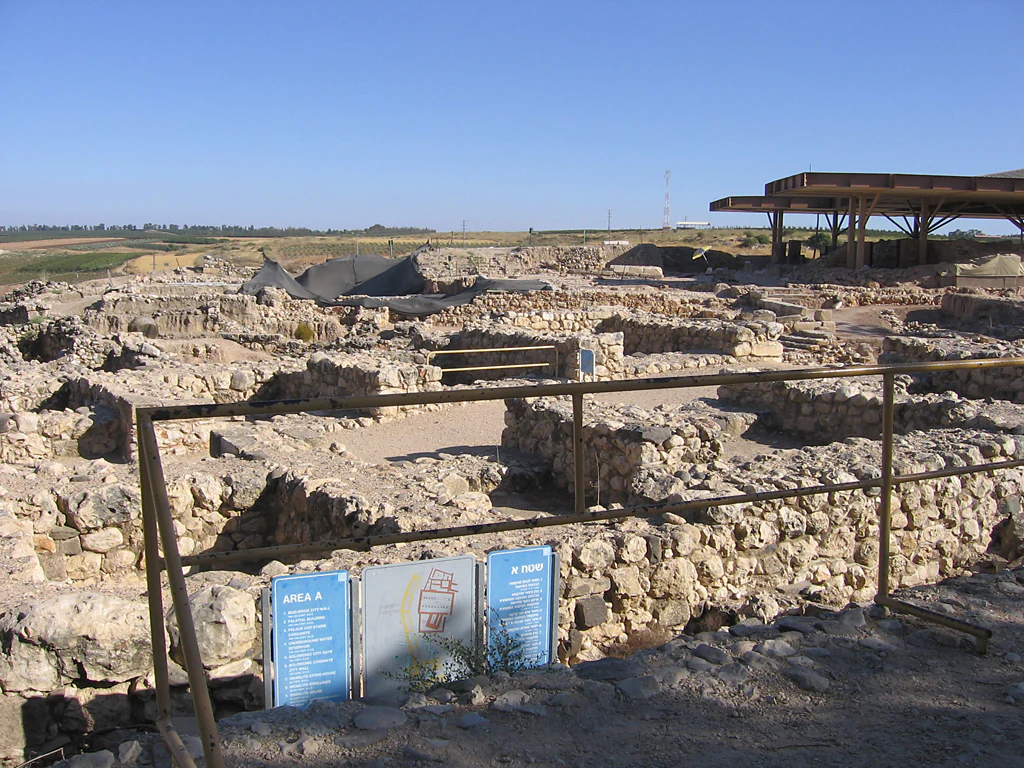 Ancient stone ruins of the Solomonic Gate at Tel Hazor National Park, with blue informational signs in the foreground and a modern shelter in the background