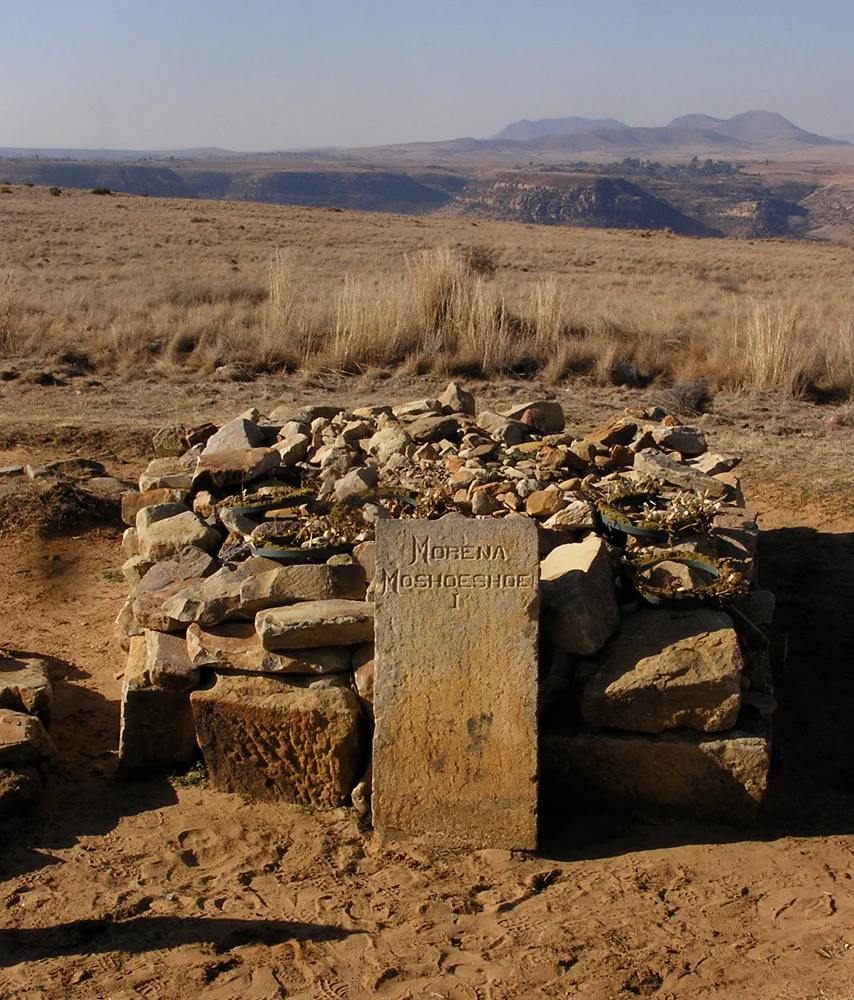 A grave marked by a stone slab engraved with the name Morena Moshoeshoe I, situated on a dry, grassy plateau with distant rolling hills.