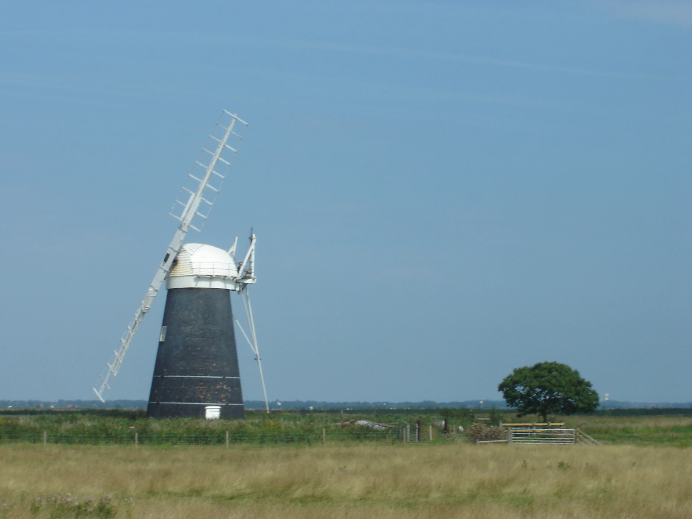 Black and white windmill with a large propeller in a grassy field under a clear blue sky