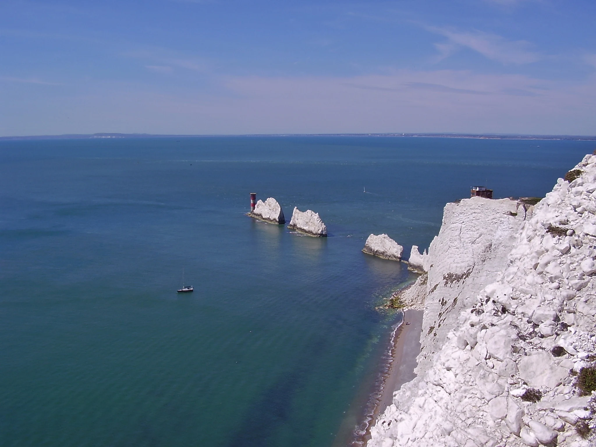 A wide angle view of the Needles chalk rock formations in the ocean, viewed from the top of the adjacent white cliffs, with a lighthouse visible on the furthest stack.