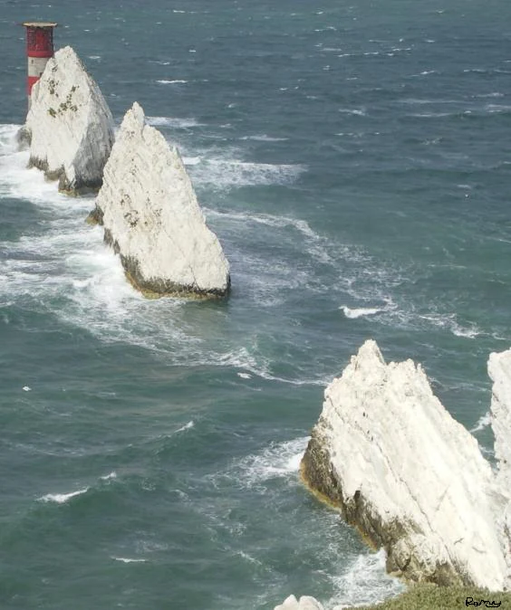 A high-angle view of the iconic Needles chalk stacks rising from the sea, with a red and white striped lighthouse situated on the outermost rock.