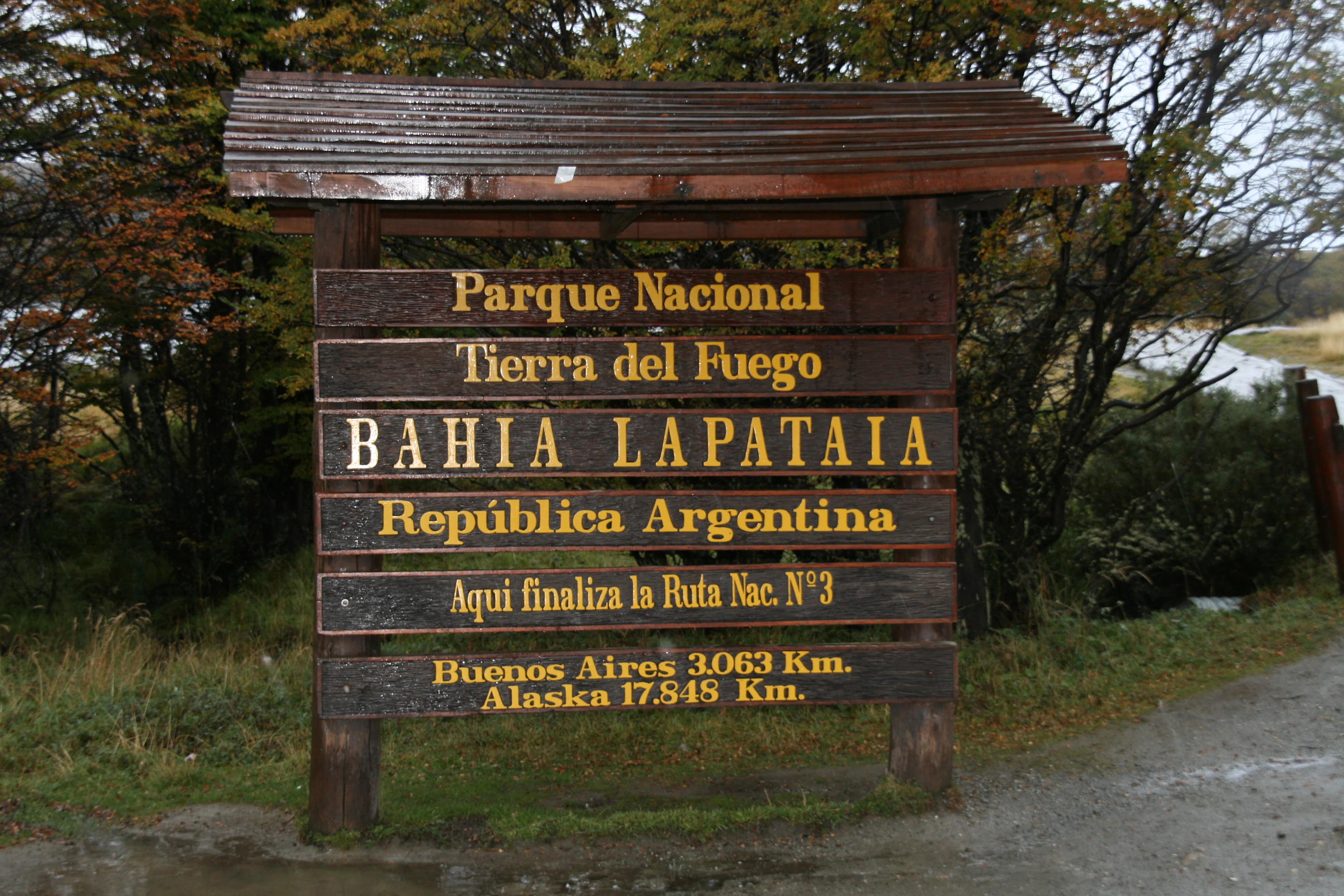 Wooden signpost displaying 'Parque Nacional Tierra del Fuego', 'Bahia Lapataia', 'Republica Argentina', and distance information to Buenos Aires and Alaska