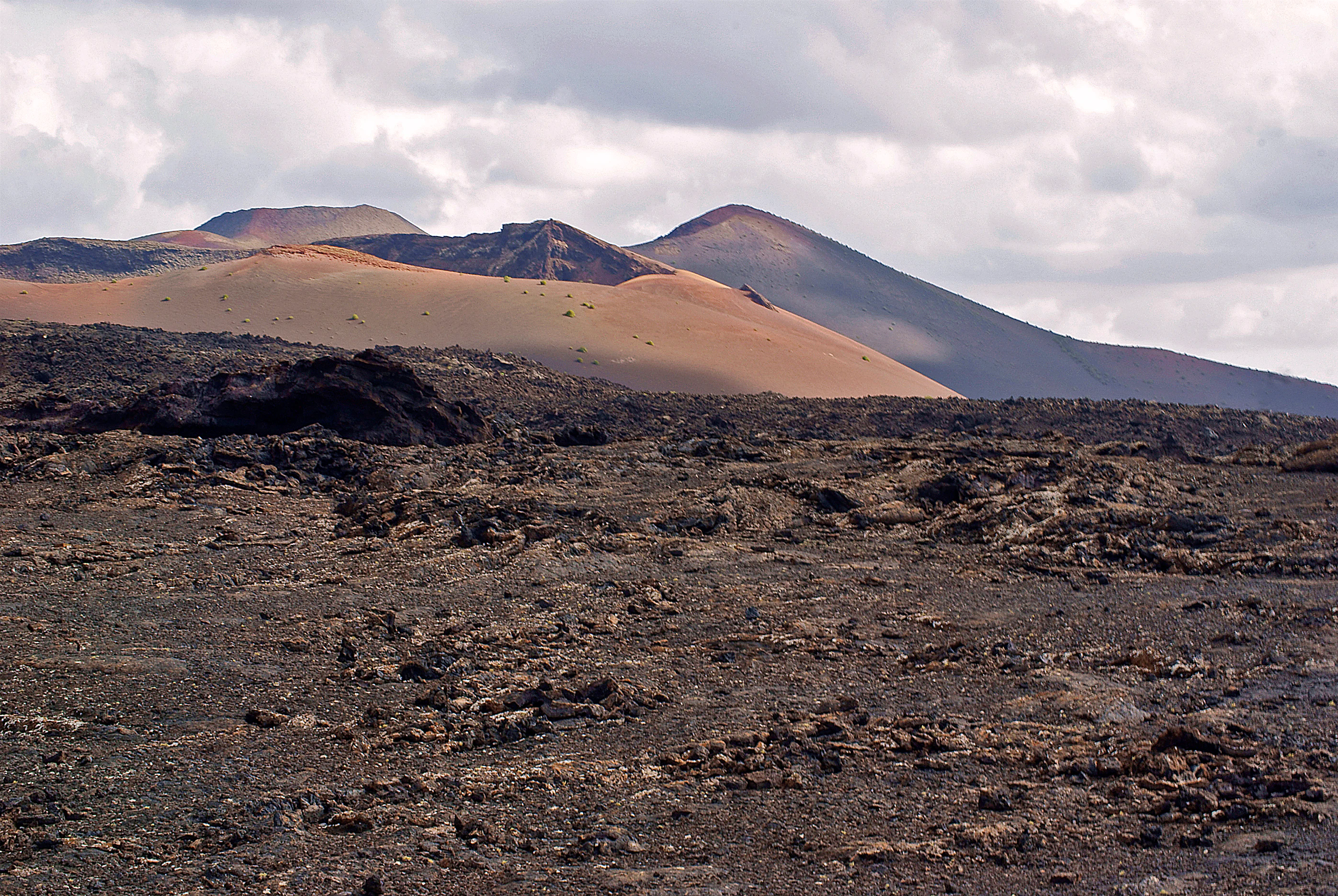 A volcanic landscape with rocky terrain, rolling hills, and mountains under a cloudy sky