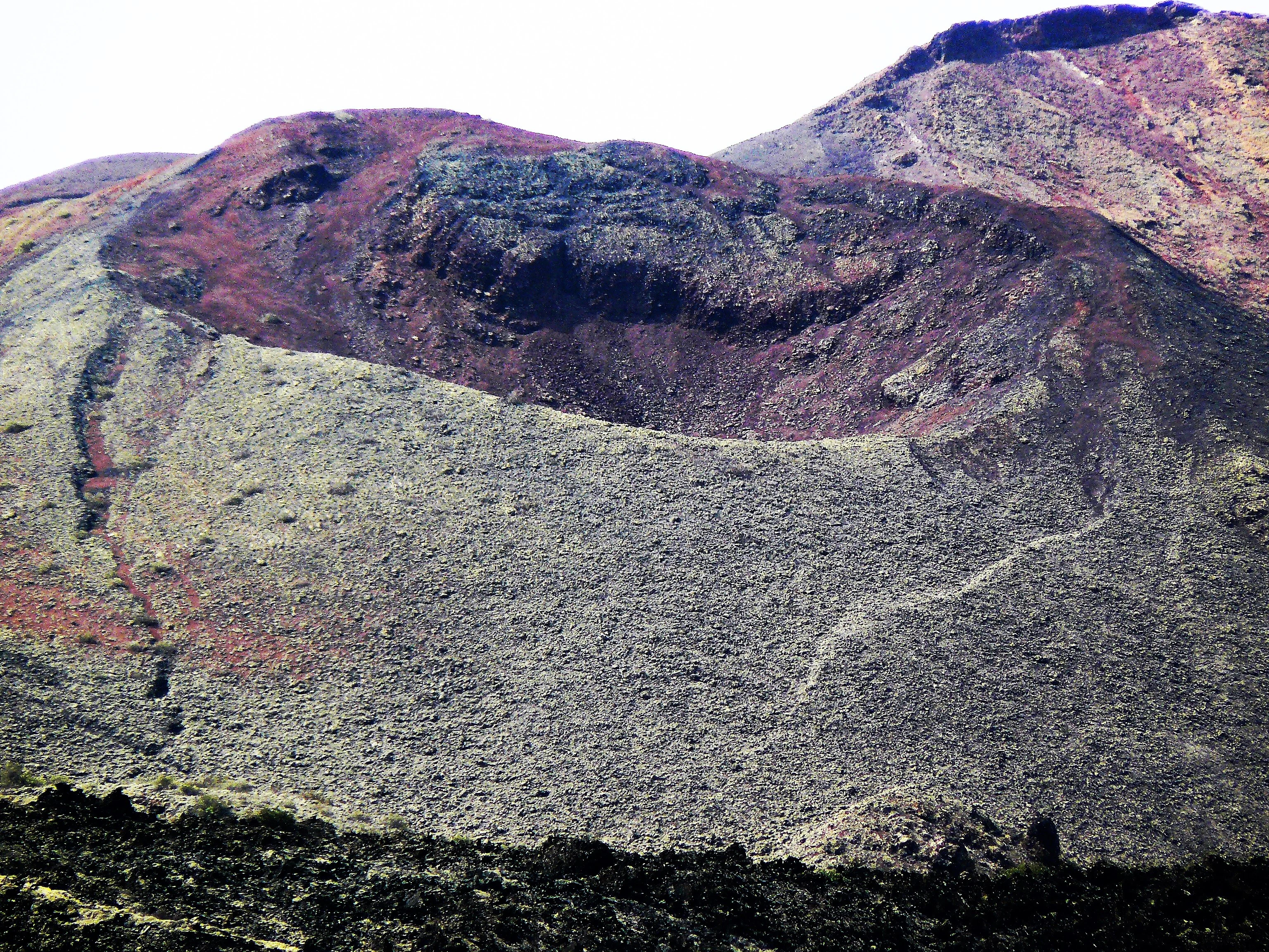 Volcanic cone with crater-like depression surrounded by rocky terrain in varying shades of brown and gray.