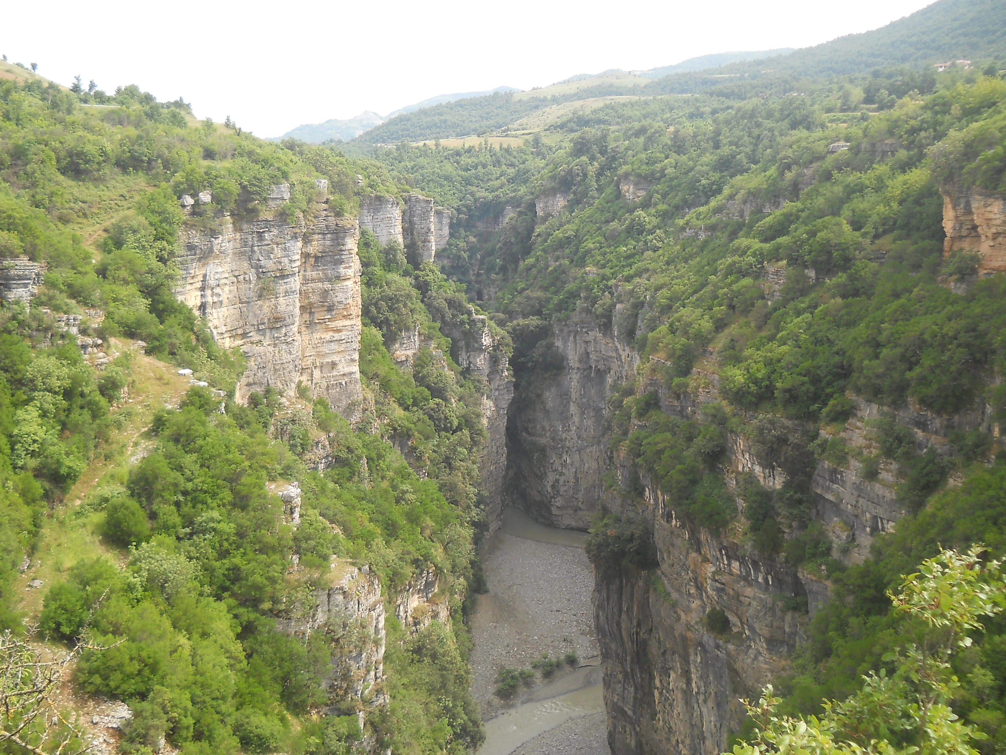 Wide view of a deep canyon with steep rock cliffs, a river below, and dense green vegetation on the slopes