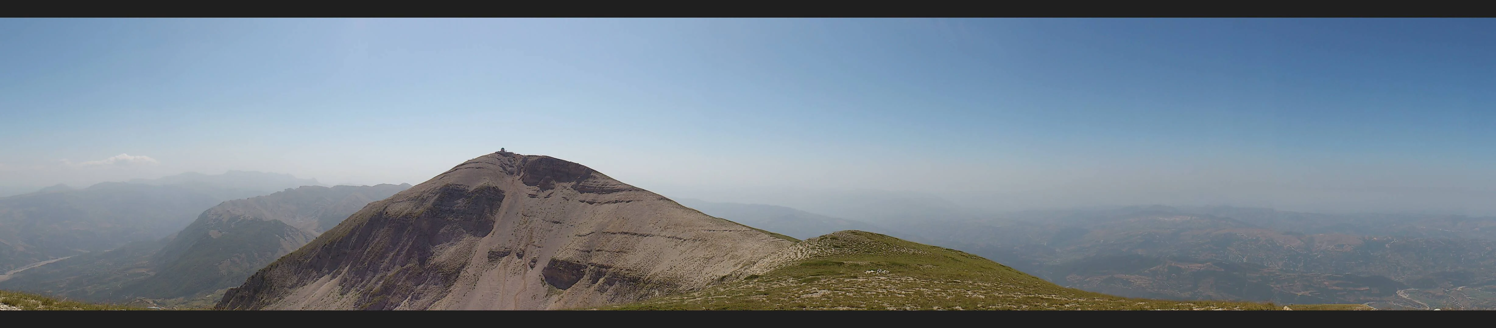 Panoramic view of Tomorr Mountain summit under a clear blue sky, showing the mountain peak and distant ranges