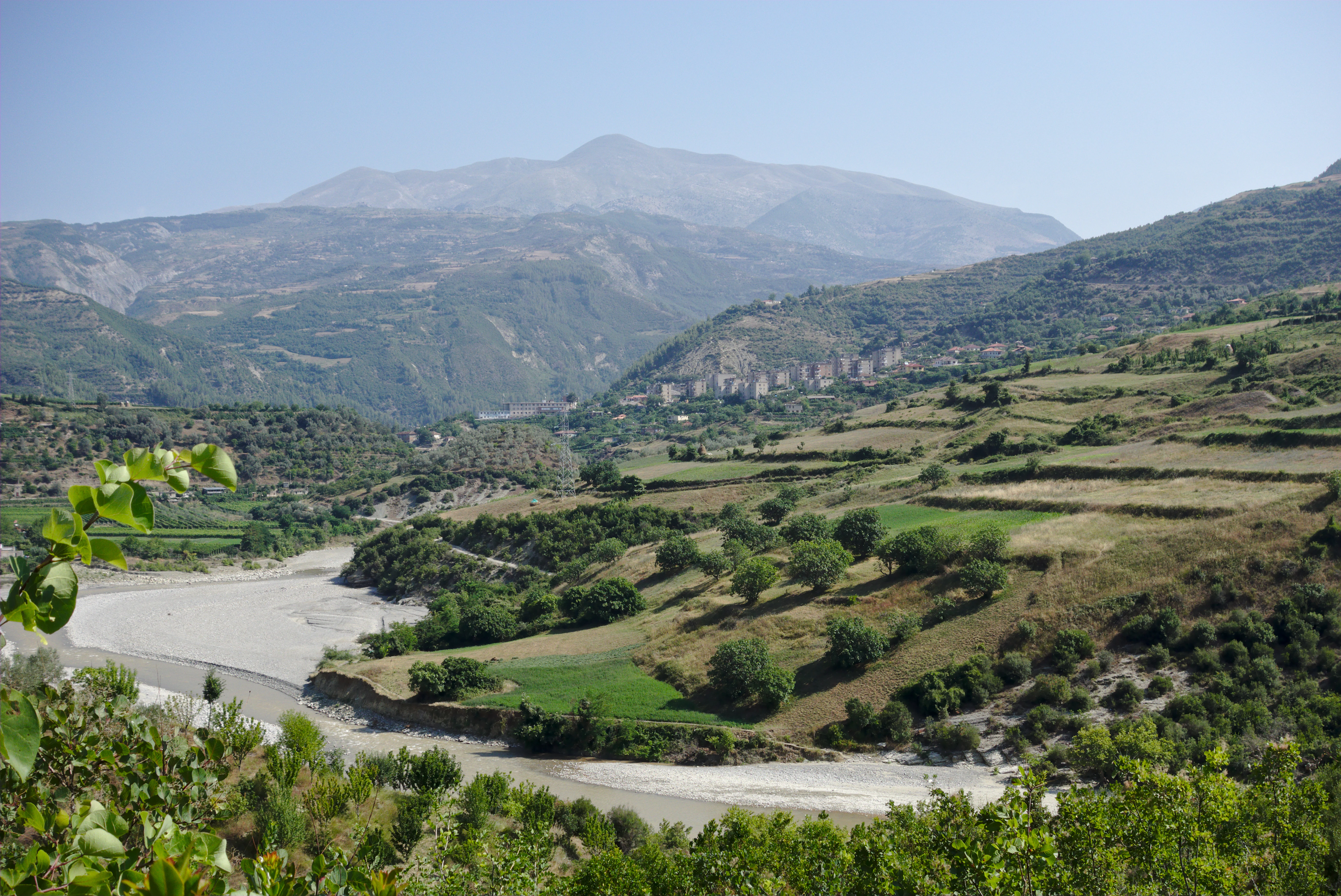 A river winding through green and brown agricultural fields with hills and a large mountain in the distance under a clear blue sky
