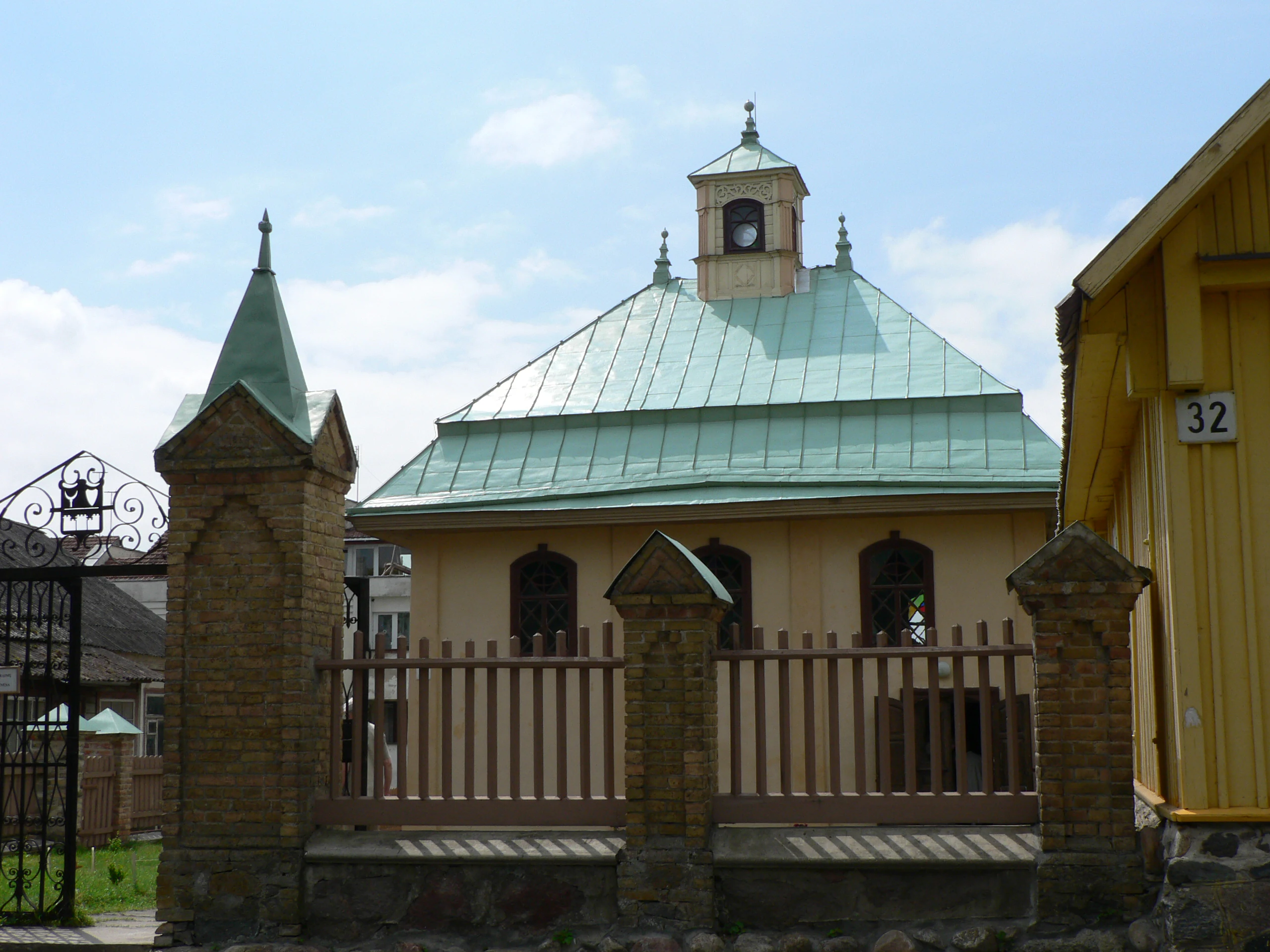 A beige building with a green copper roof, stone spires, and a wooden fence, located in Trakai National Historic Park
