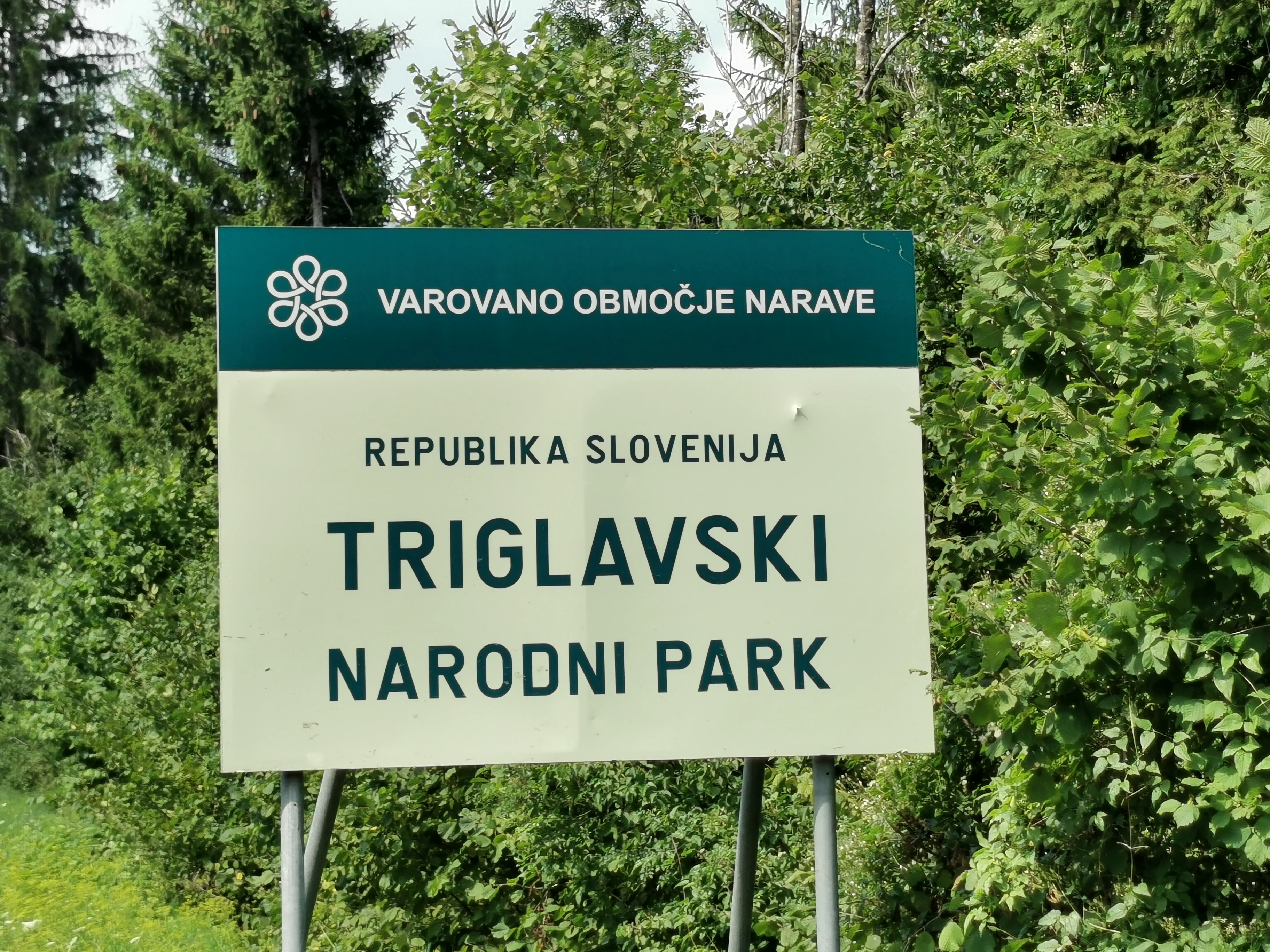Green and white sign for Triglav National Park in Slovenia surrounded by green foliage and trees
