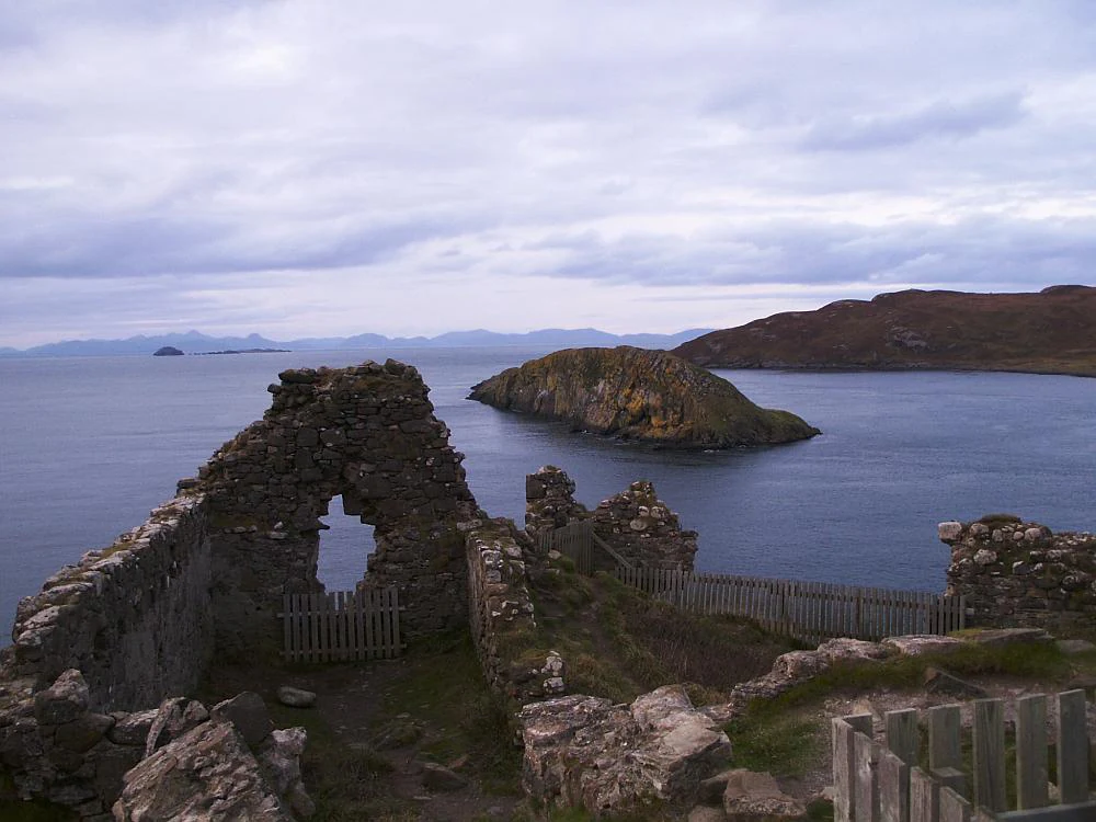Stone ruins of Duntulm Castle overlooking the sea and a nearby offshore island under a cloudy sky.
