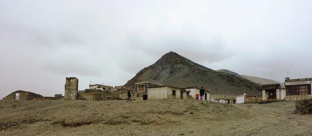 A wide view of a small, rustic village in a dry, mountainous region under a cloudy sky.