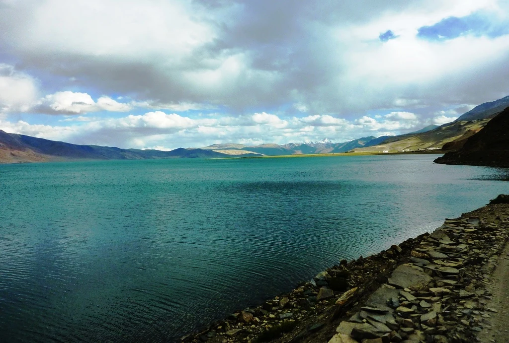Vista panorámica del paisaje de Tso Moriri, un vasto lago de gran altitud con aguas turquesas rodeado de montañas áridas bajo un cielo nublado.