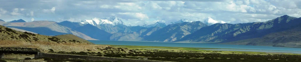 Vista panorámica de un vasto y tranquilo lago turquesa situado bajo altas cadenas montañosas con picos nevados bajo un cielo nublado.