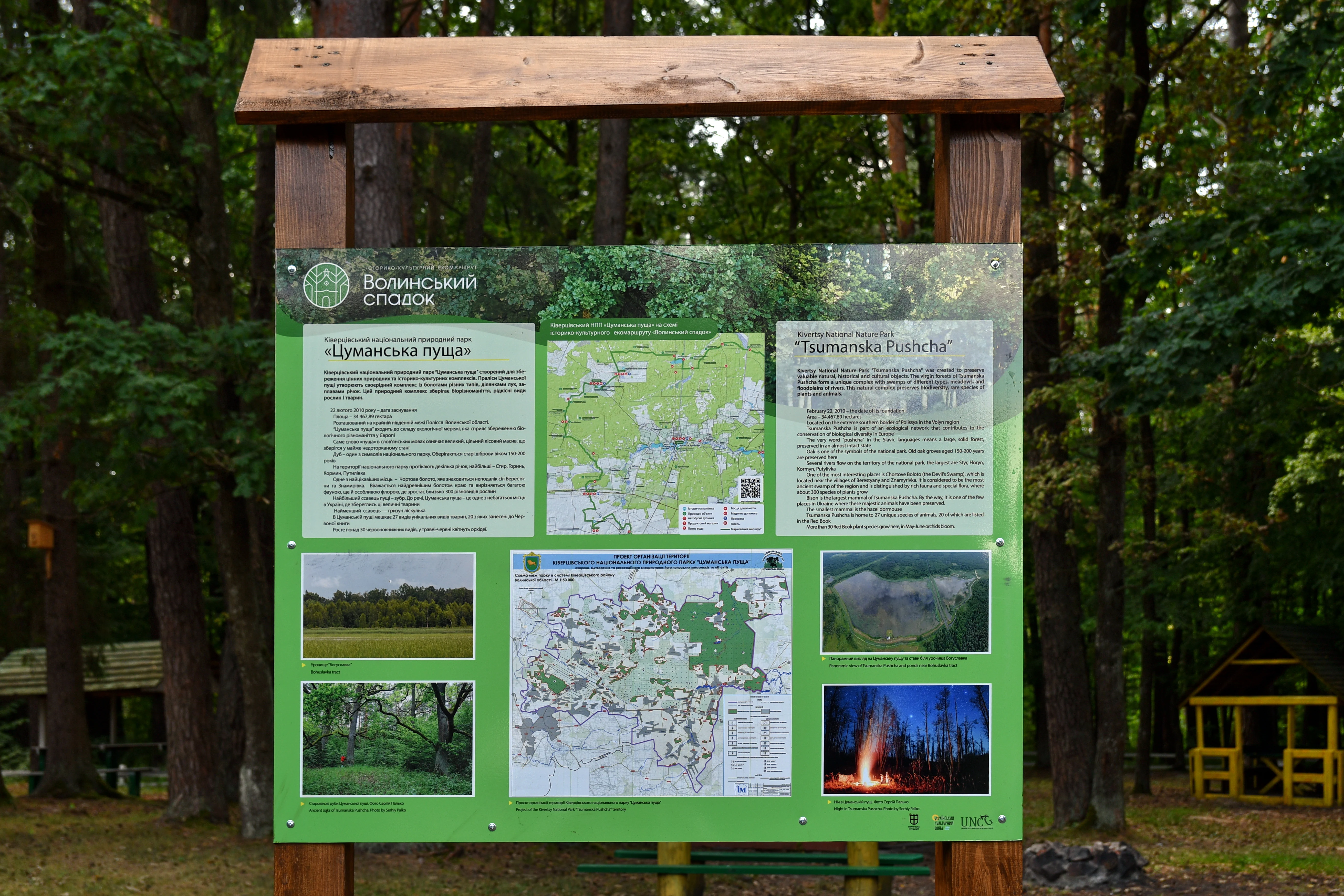 Green information board mounted on wooden posts displaying text, maps, and photographs related to Tsumanska Pushcha National Nature Park