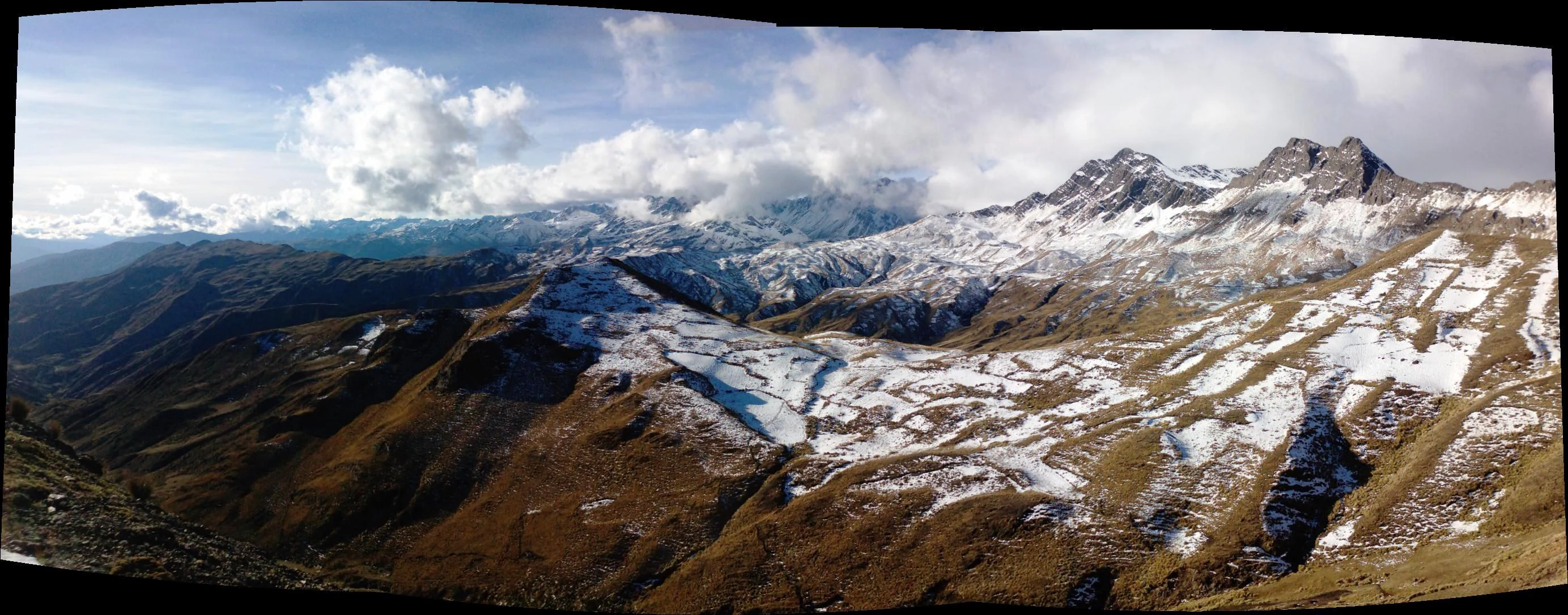 Panoramic landscape of snow-covered mountain peaks and rocky valleys under a partly cloudy sky